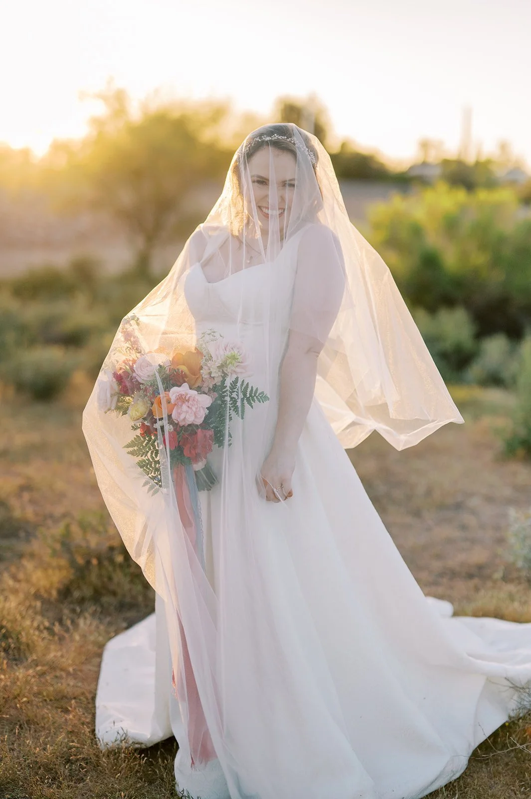 Bride holding a bright garden-style wedding bouquet with colorful pink, yellow, orange and red flowers.