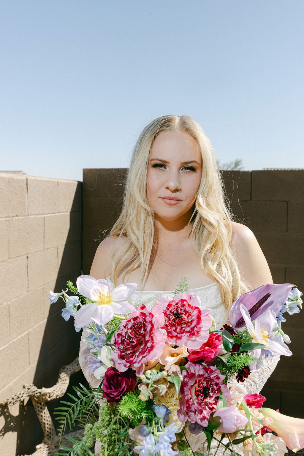 Colorful garden-style wedding arrangement featuring bright pink, yellow, purple and blue flowers with trailing greenery.