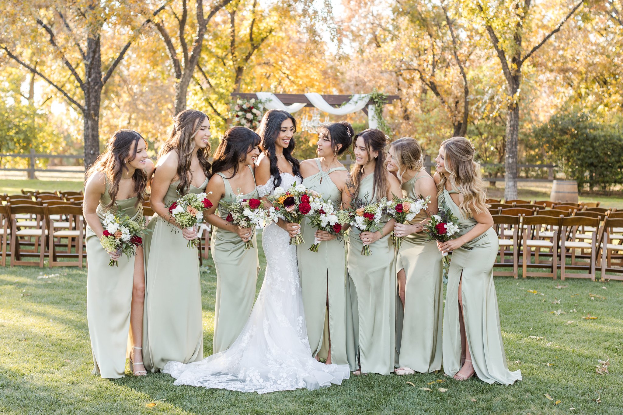 Bride and bridesmaids in sage green dresses holding romantic fall wedding bouquets with burgundy and peach flowers.