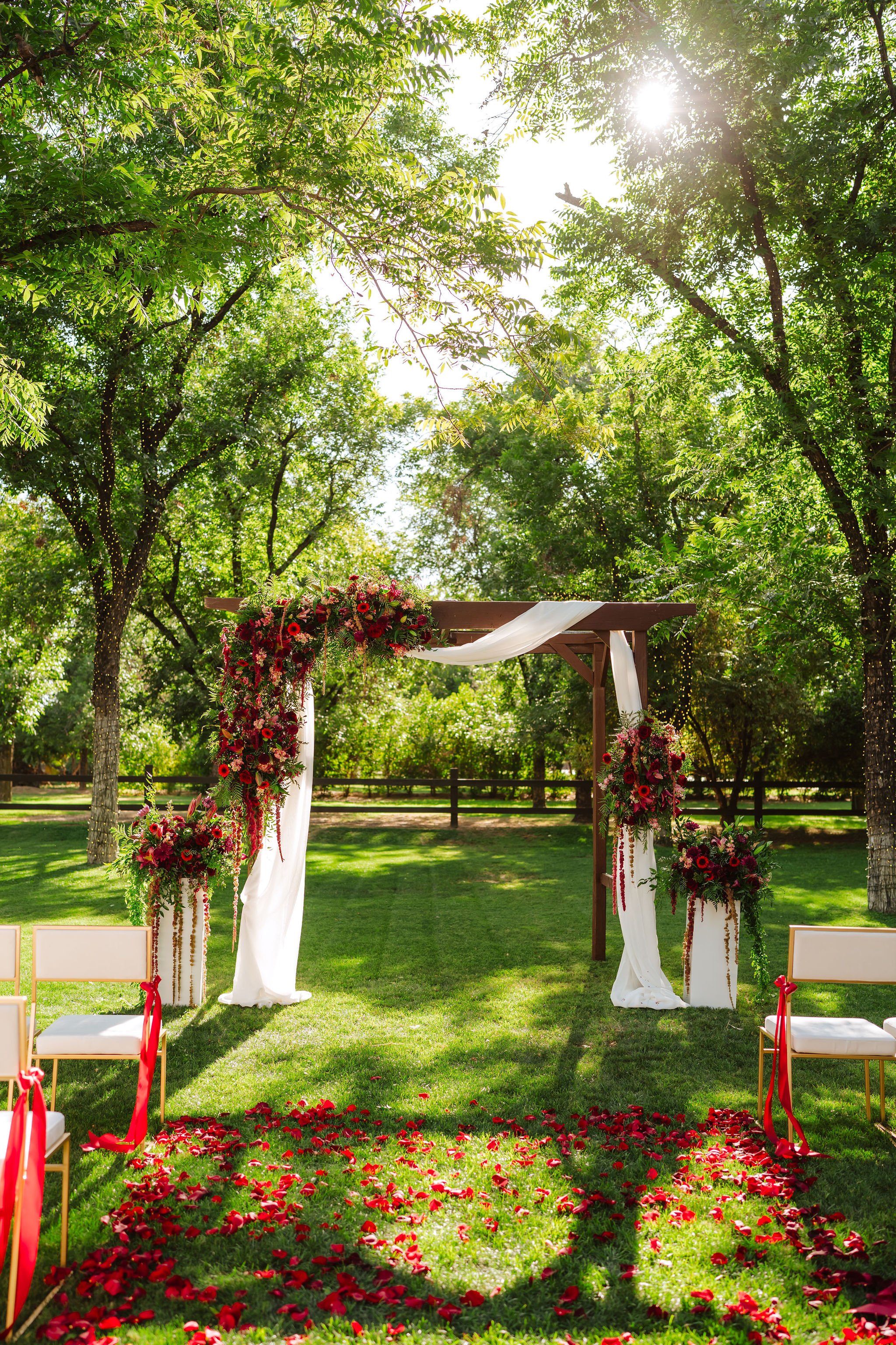 Outdoor wedding ceremony at Venue at the Grove framed by dramatic red and burgundy floral installations.
