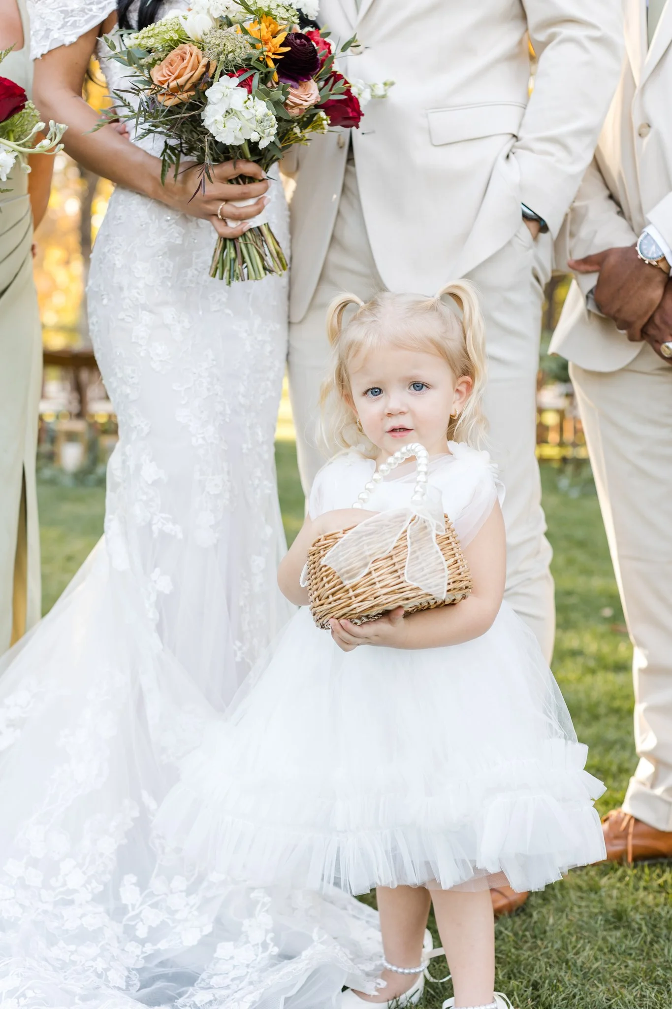 Flower girl carrying a small basket during an outdoor garden wedding ceremony.