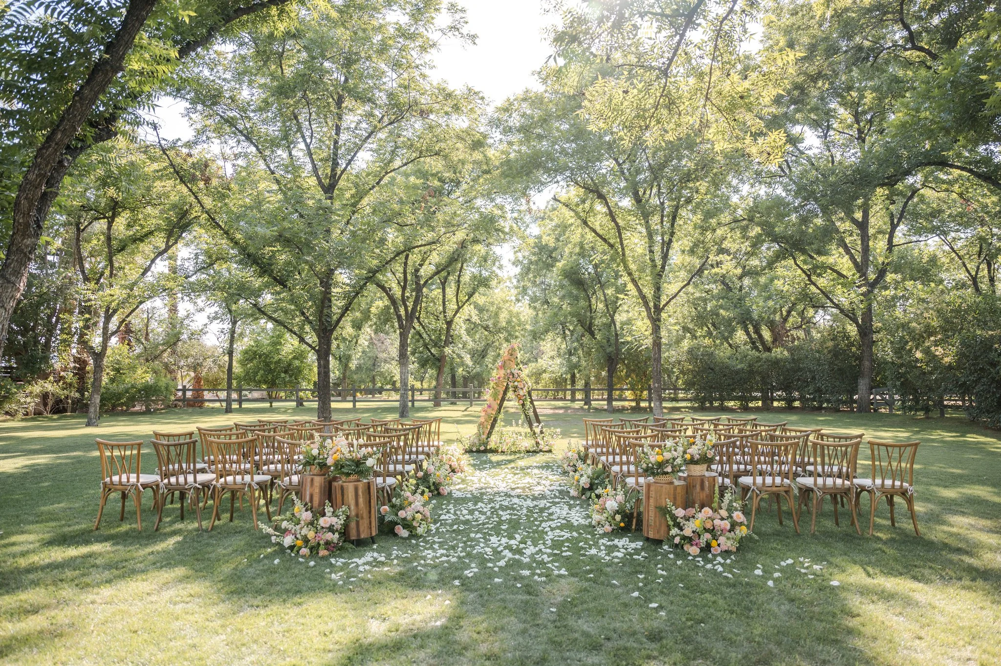 Outdoor wedding ceremony at Venue at the Grove with colorful garden flowers lining the aisle and floral ceremony installations beneath mature trees.