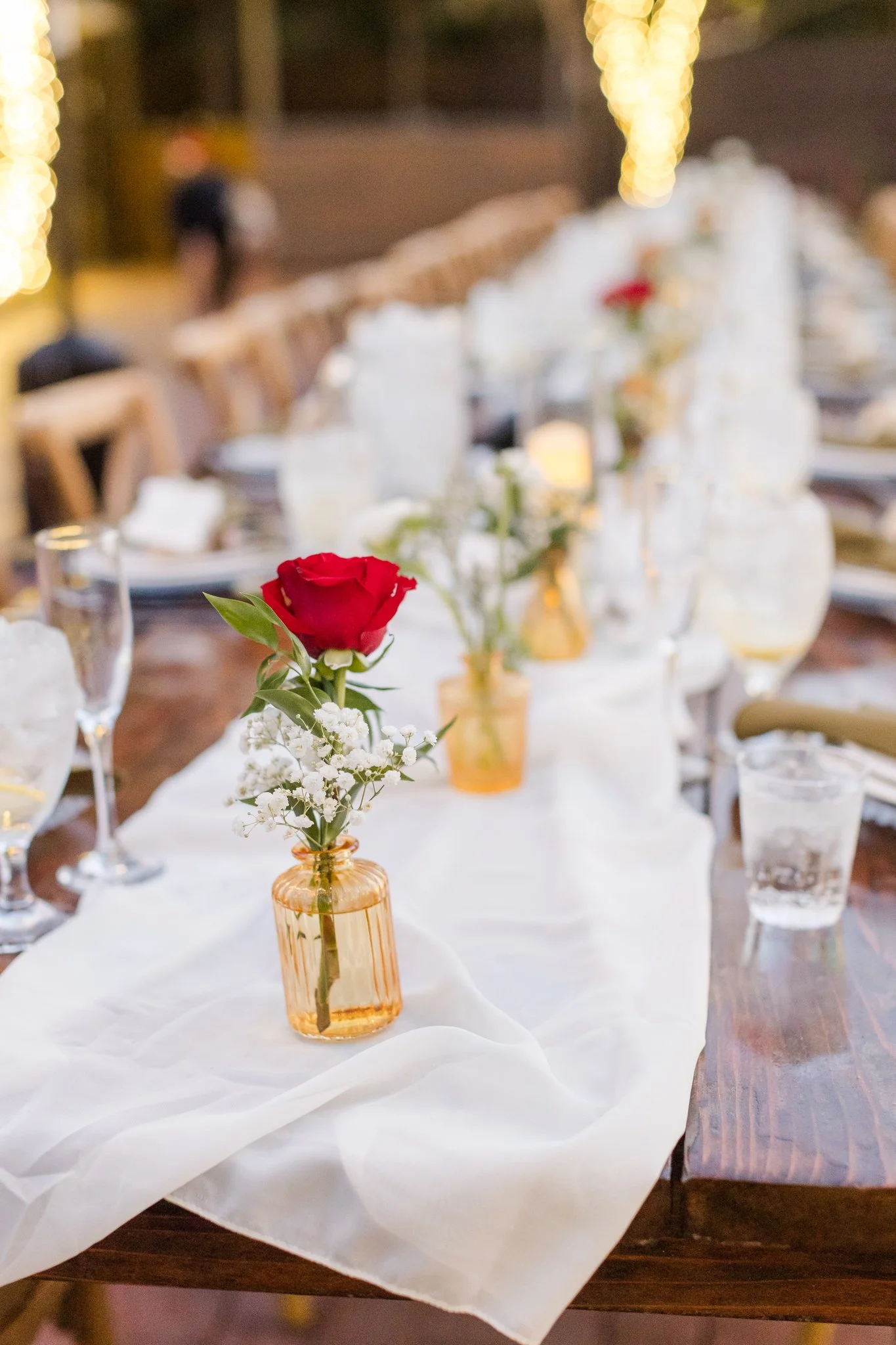 Romantic fall wedding reception centerpiece with red and peach flowers in an amber bud vase.