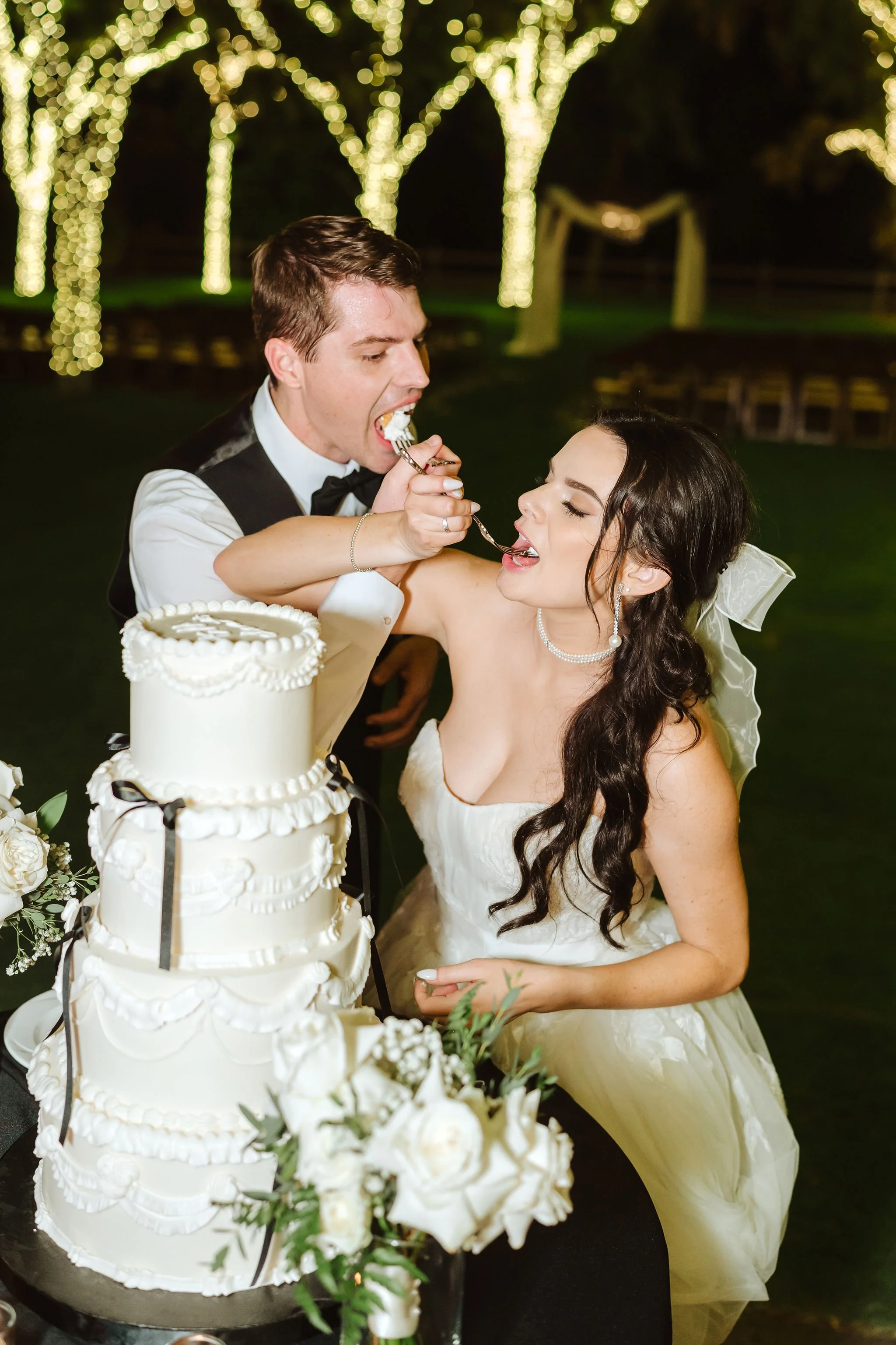 Bride and groom cutting their wedding cake surrounded by elegant white and green reception florals.