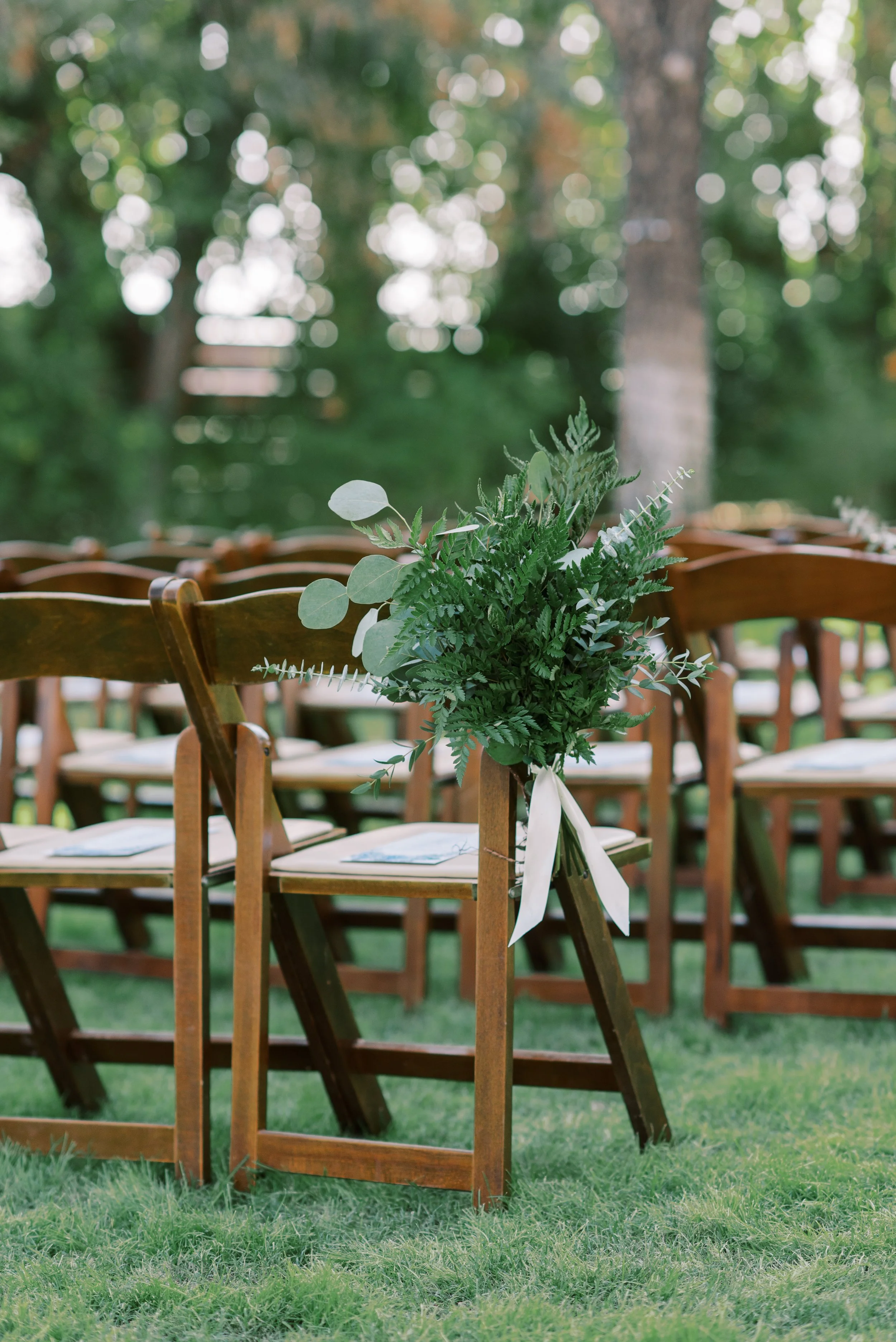 Wedding aisle chairs decorated with soft white flowers and organic greenery for an outdoor garden ceremony.