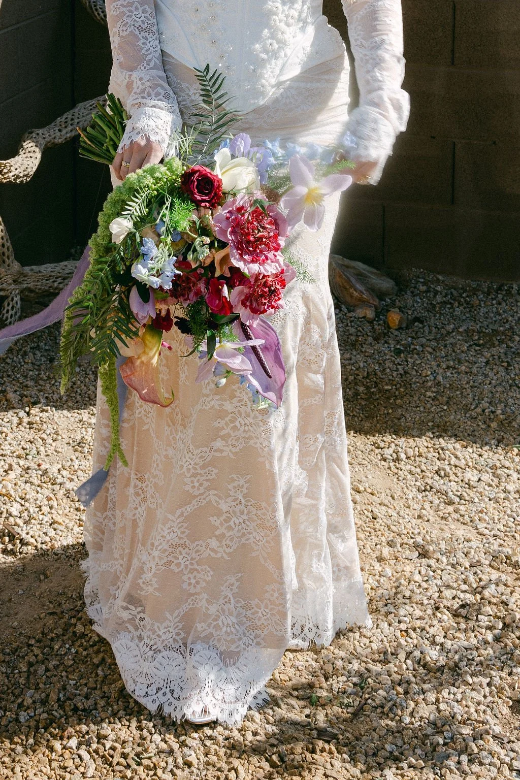 Bride holding a cascading colorful wedding bouquet with vibrant pink, purple and red flowers.