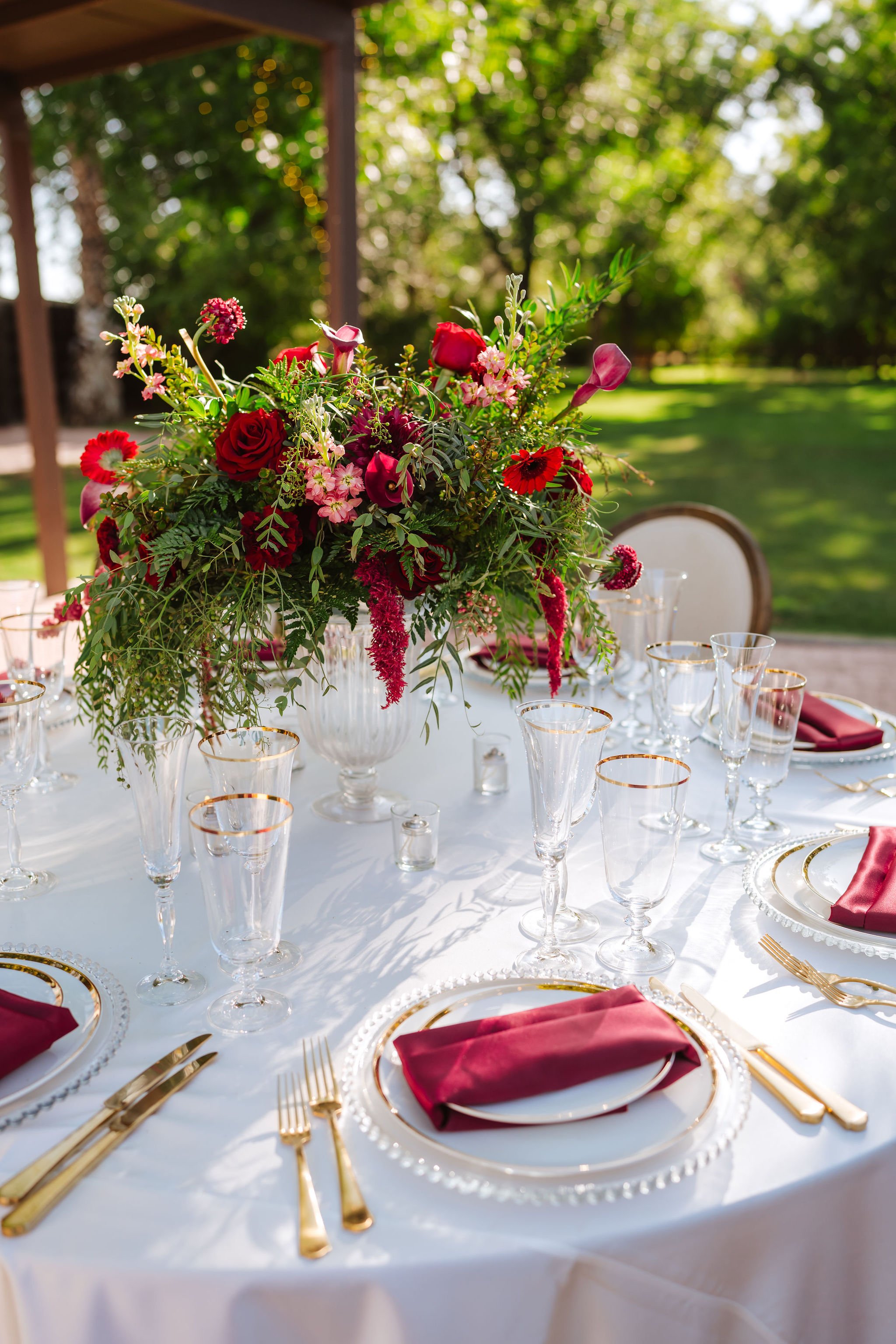 Elevated red and burgundy wedding centerpiece with lush flowers and greenery above an elegant reception table.