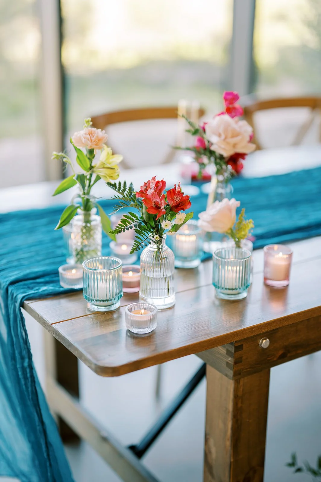 Colorful bud vase wedding centerpieces with bright flowers and candles on a modern reception table.