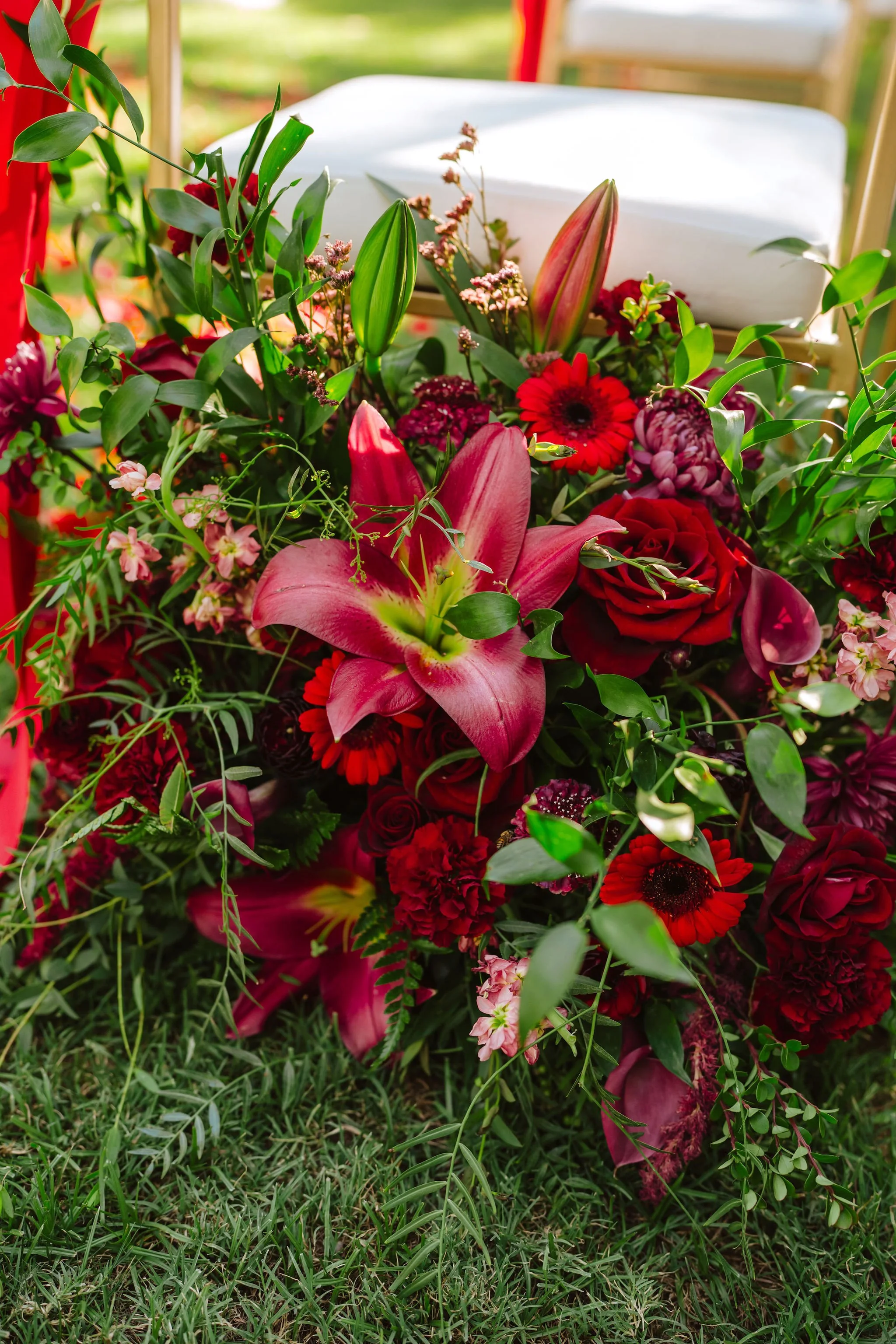 Close-up of lush burgundy, red and pink wedding flowers featuring roses, lilies and textural greenery.