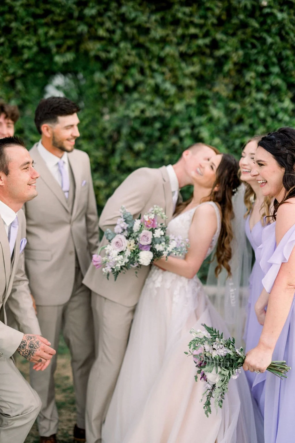Bride and groom celebrating with their wedding party while holding romantic lavender and blush floral bouquets.