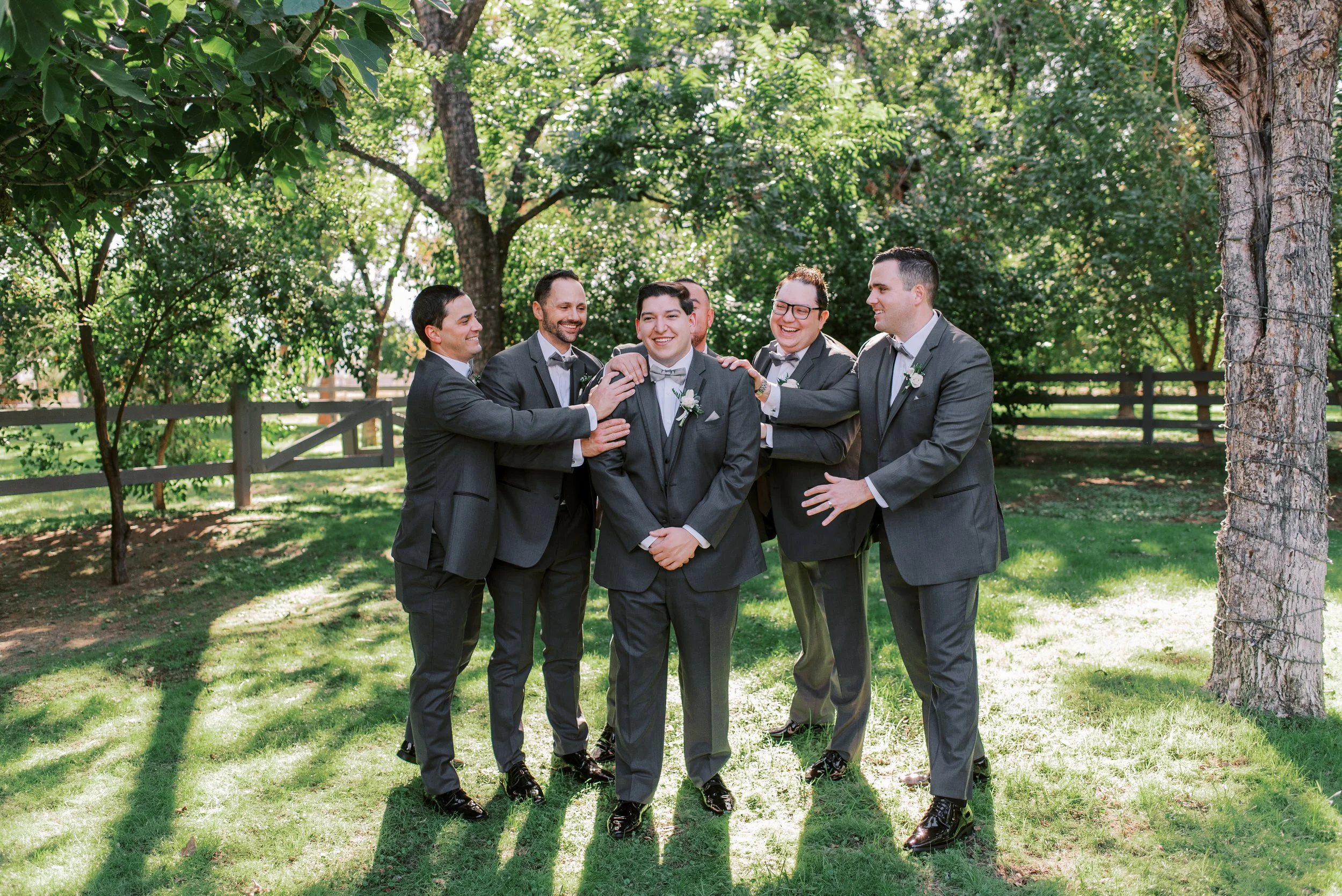 Groom and groomsmen in classic black suits beneath the trees at a Venue at the Grove wedding.