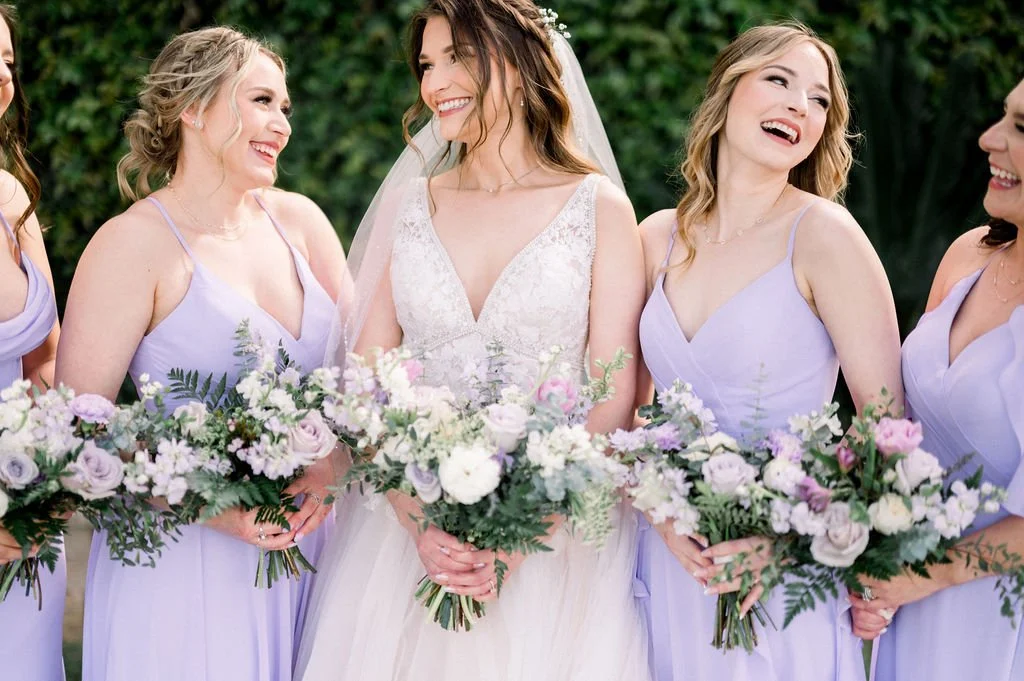 Bride and bridesmaids carrying lavender, pink and white garden-inspired wedding bouquets with organic greenery.