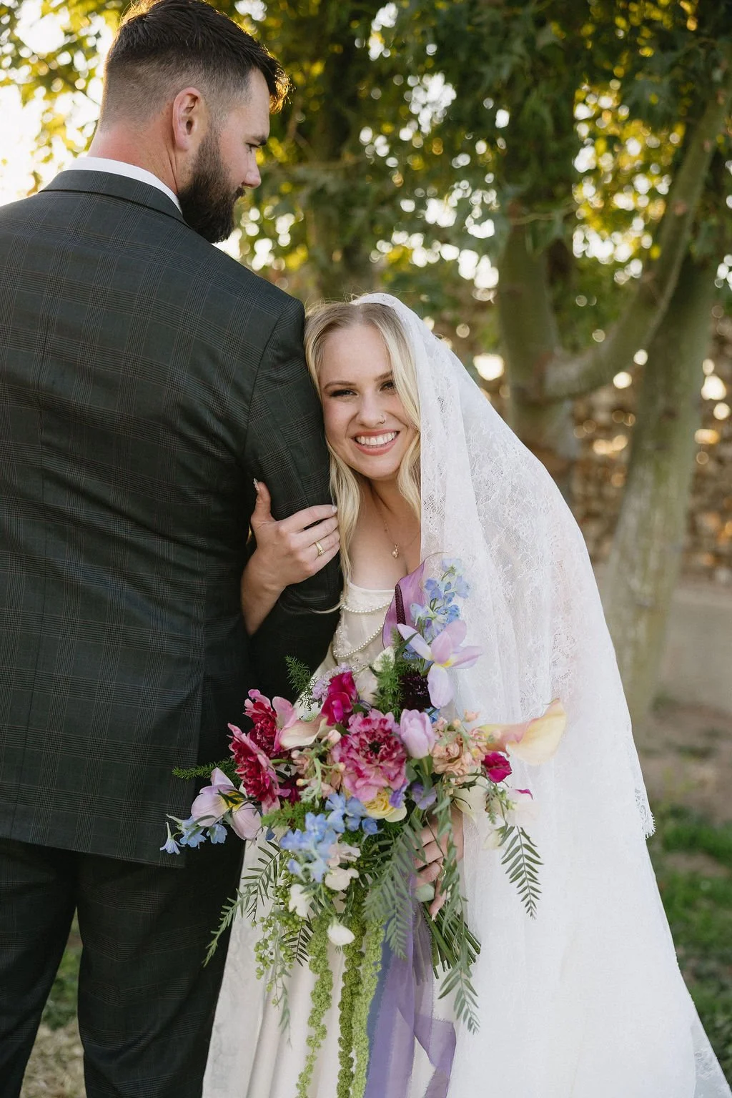 Bride holding a vibrant garden-style bouquet filled with pink, purple and colorful seasonal wedding flowers.