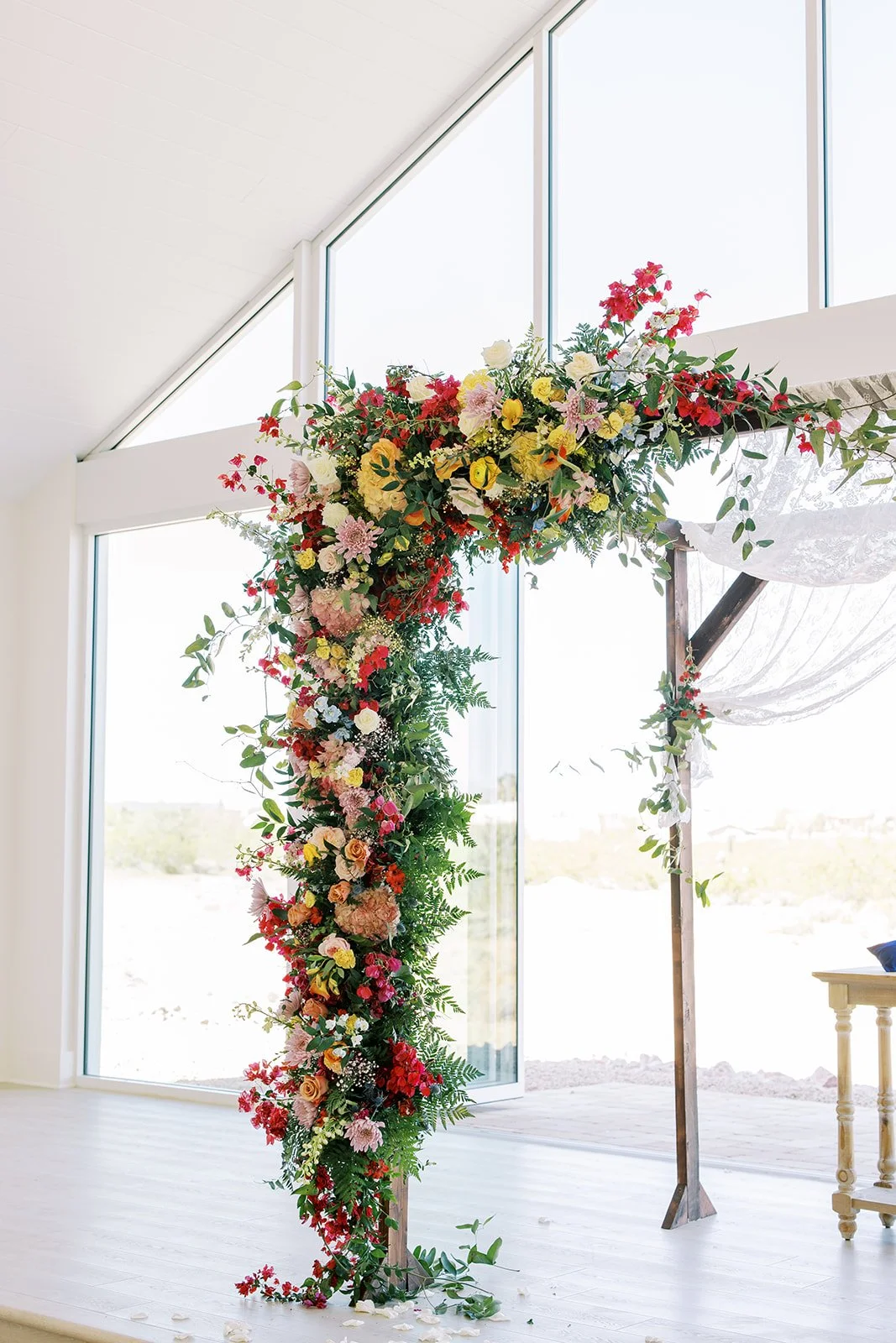 Colorful wedding ceremony arch covered in vibrant red, pink and yellow flowers with lush greenery at Desert View.