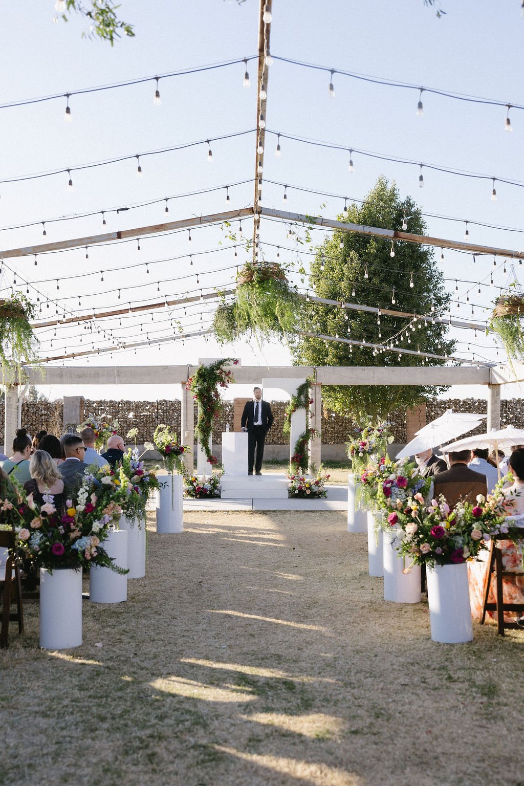 Colorful floral installation with pink and burgundy flowers cascading along a white backyard wedding structure.