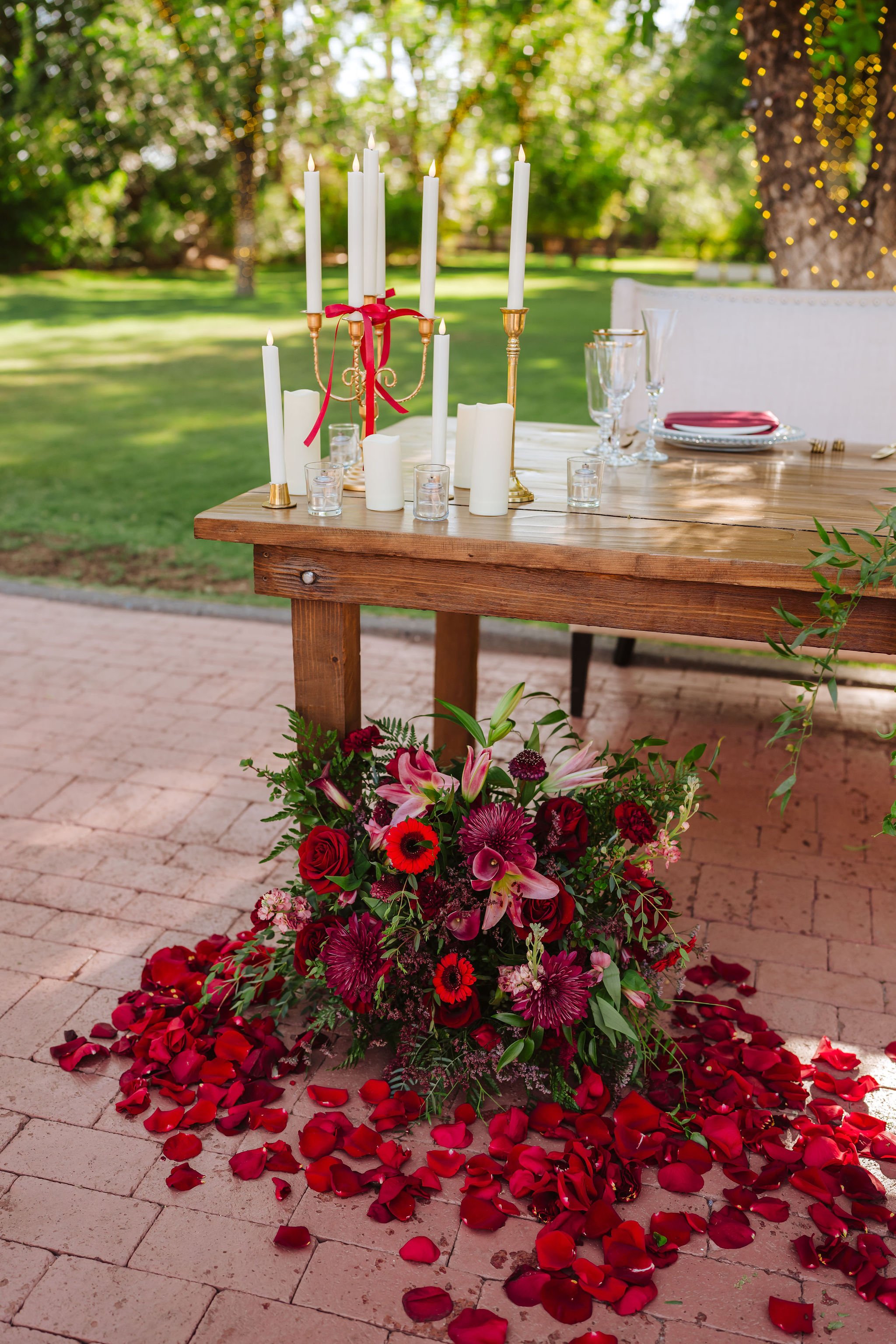 Low red and burgundy wedding floral arrangement with rich roses and greenery beside a modern reception lounge.