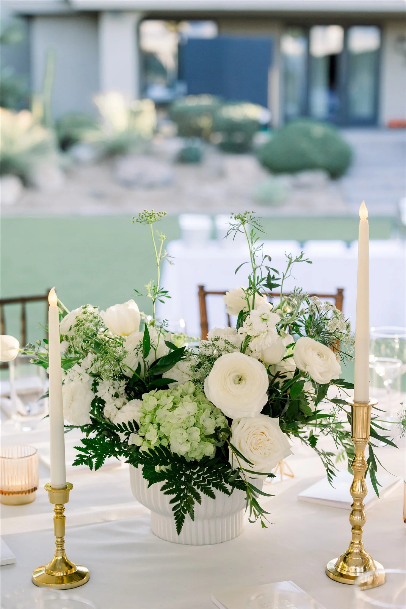 White and green wedding reception centerpiece with garden-style flowers and taper candles.