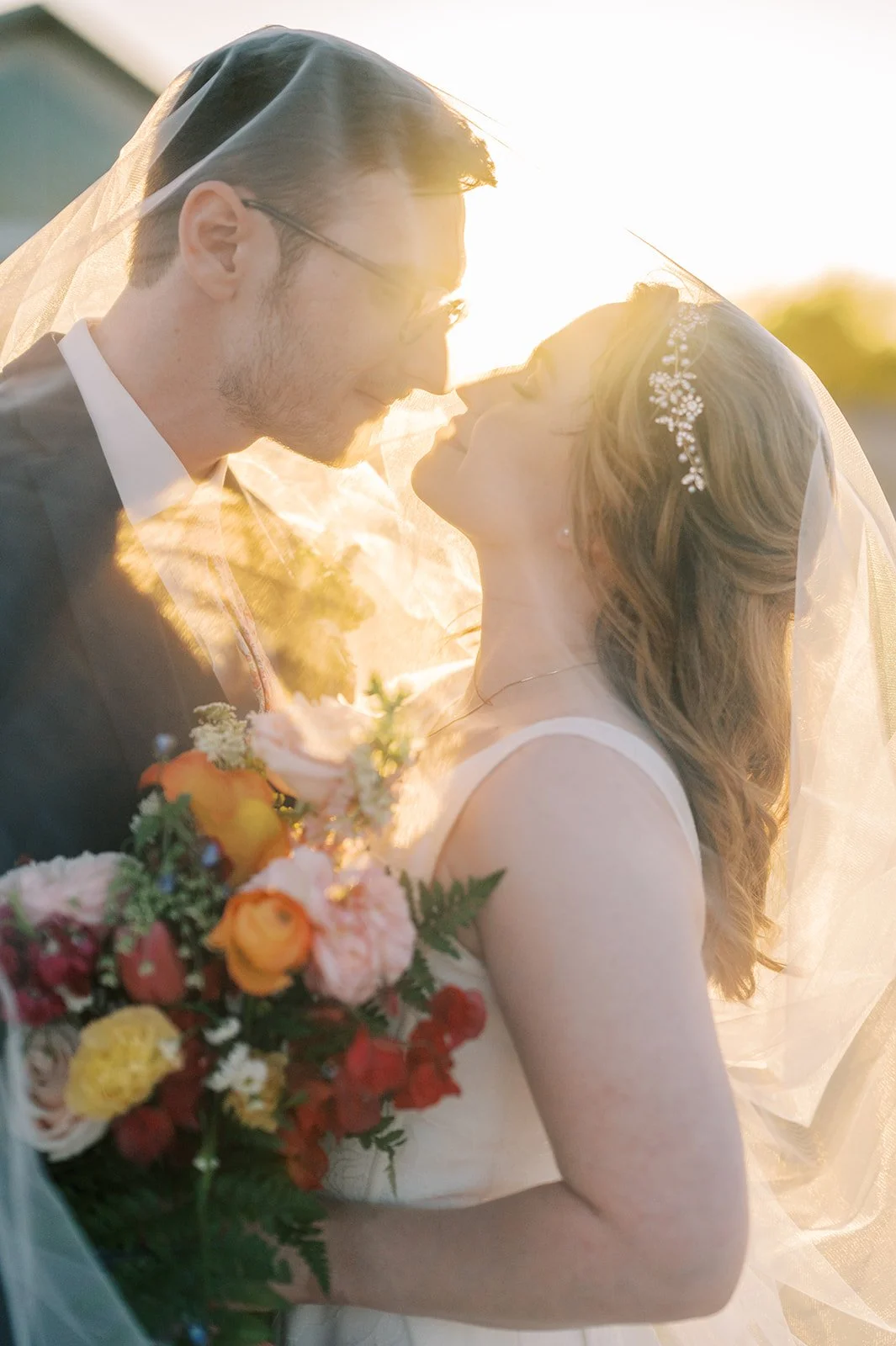 Bride and groom holding a vibrant colorful wedding bouquet during golden hour.