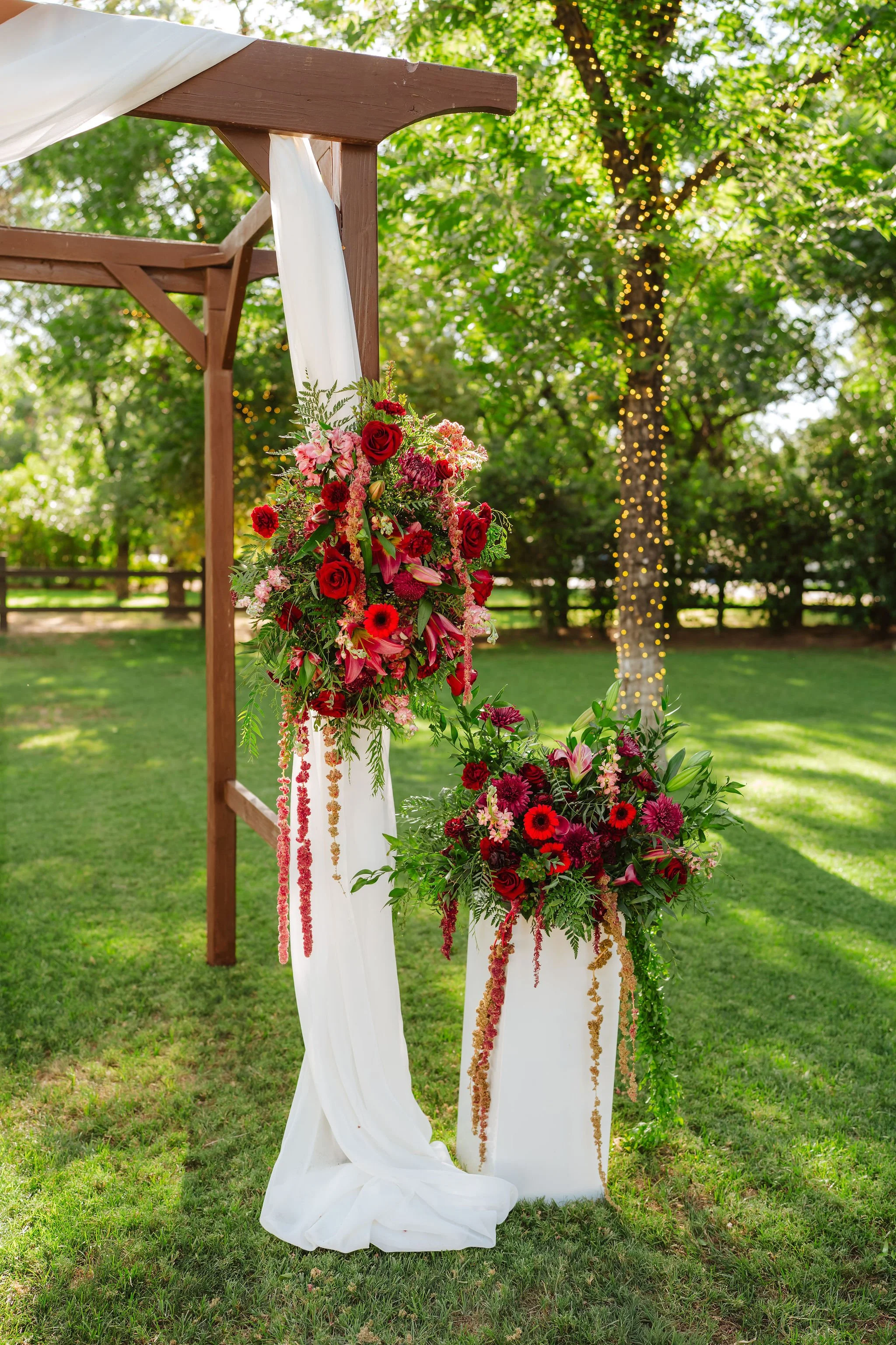 Romantic red and burgundy floral installation attached to a wooden wedding ceremony arch at Venue at the Grove.