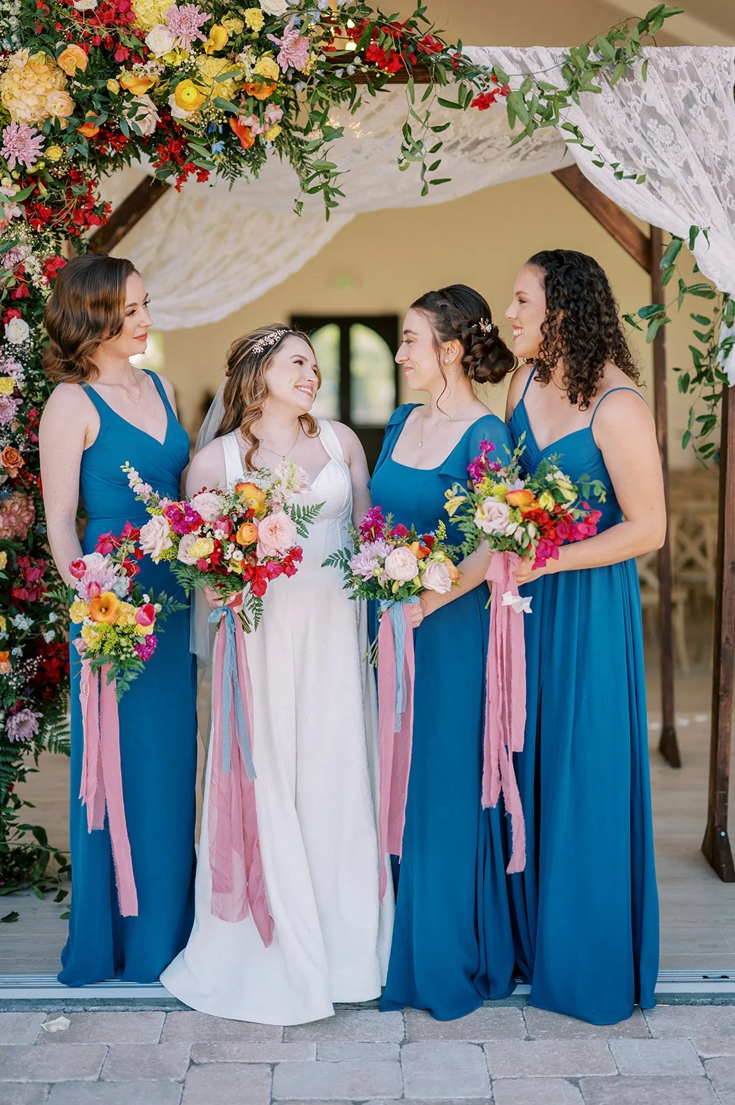 Bridesmaids holding vibrant garden-style bouquets filled with pink, red, yellow and orange wedding flowers.