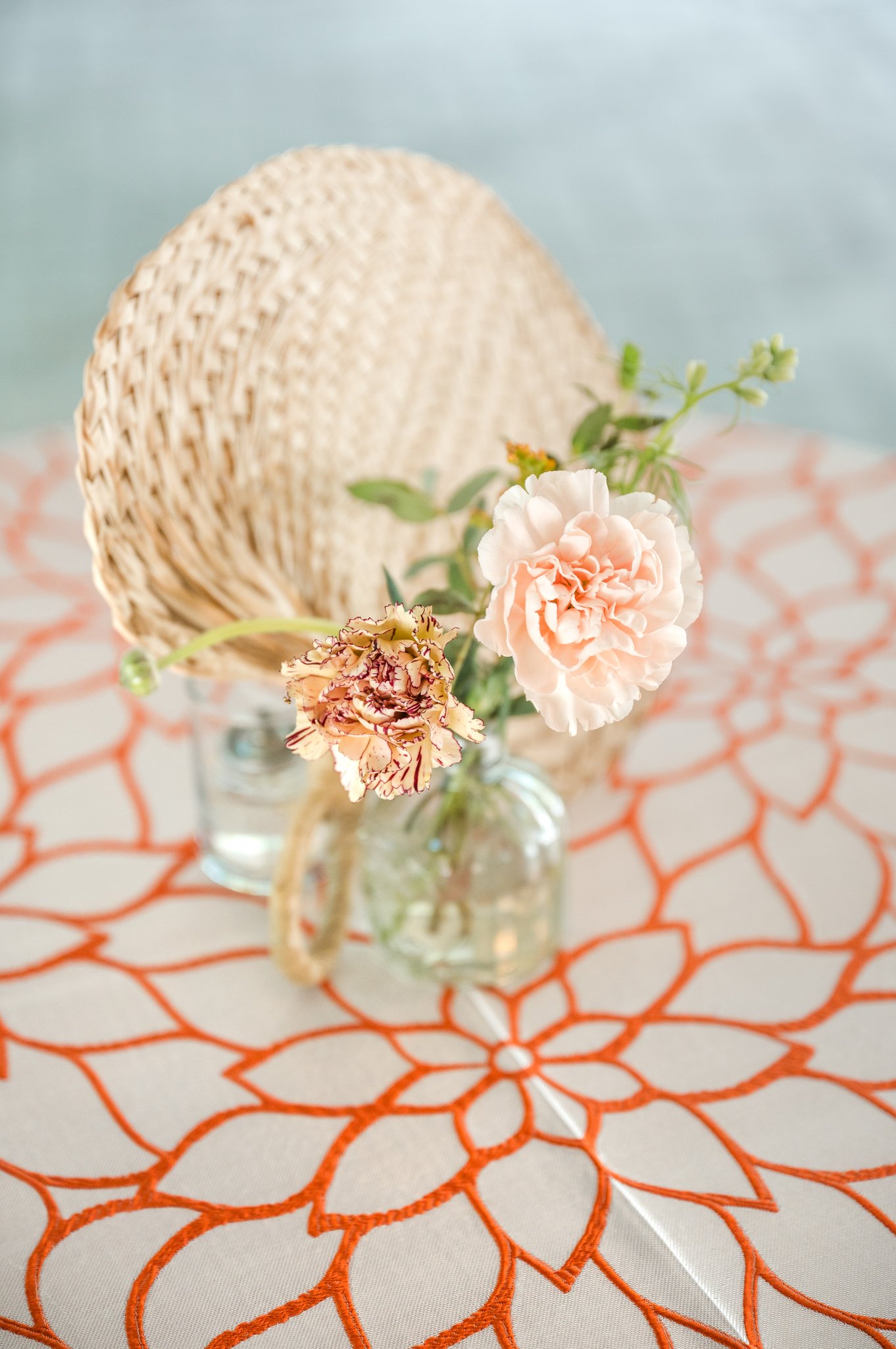 Small garden-style wedding centerpiece with peach flowers and greenery on a colorful reception table.