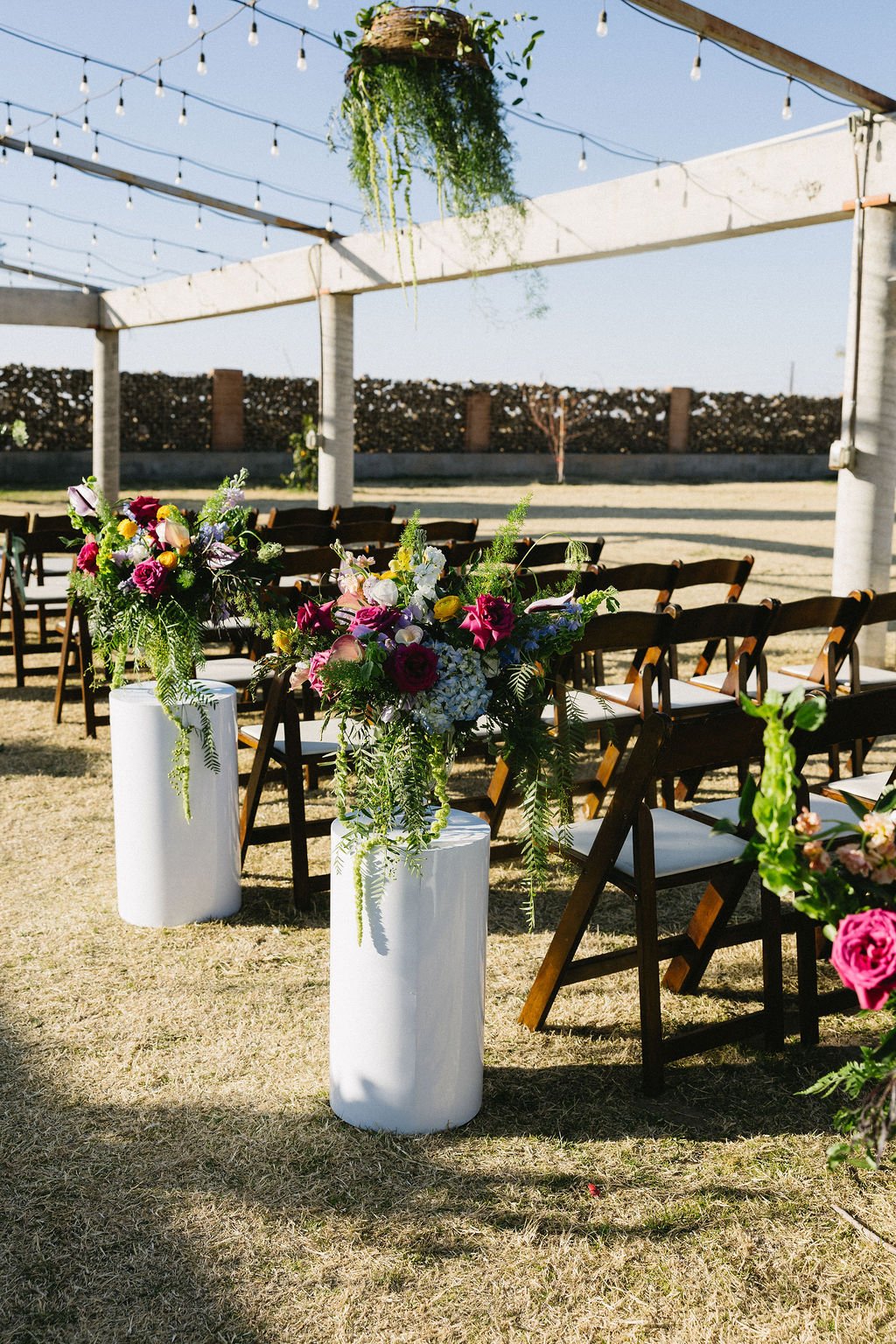 Outdoor backyard wedding reception with colorful floral arrangements lining long dinner tables.