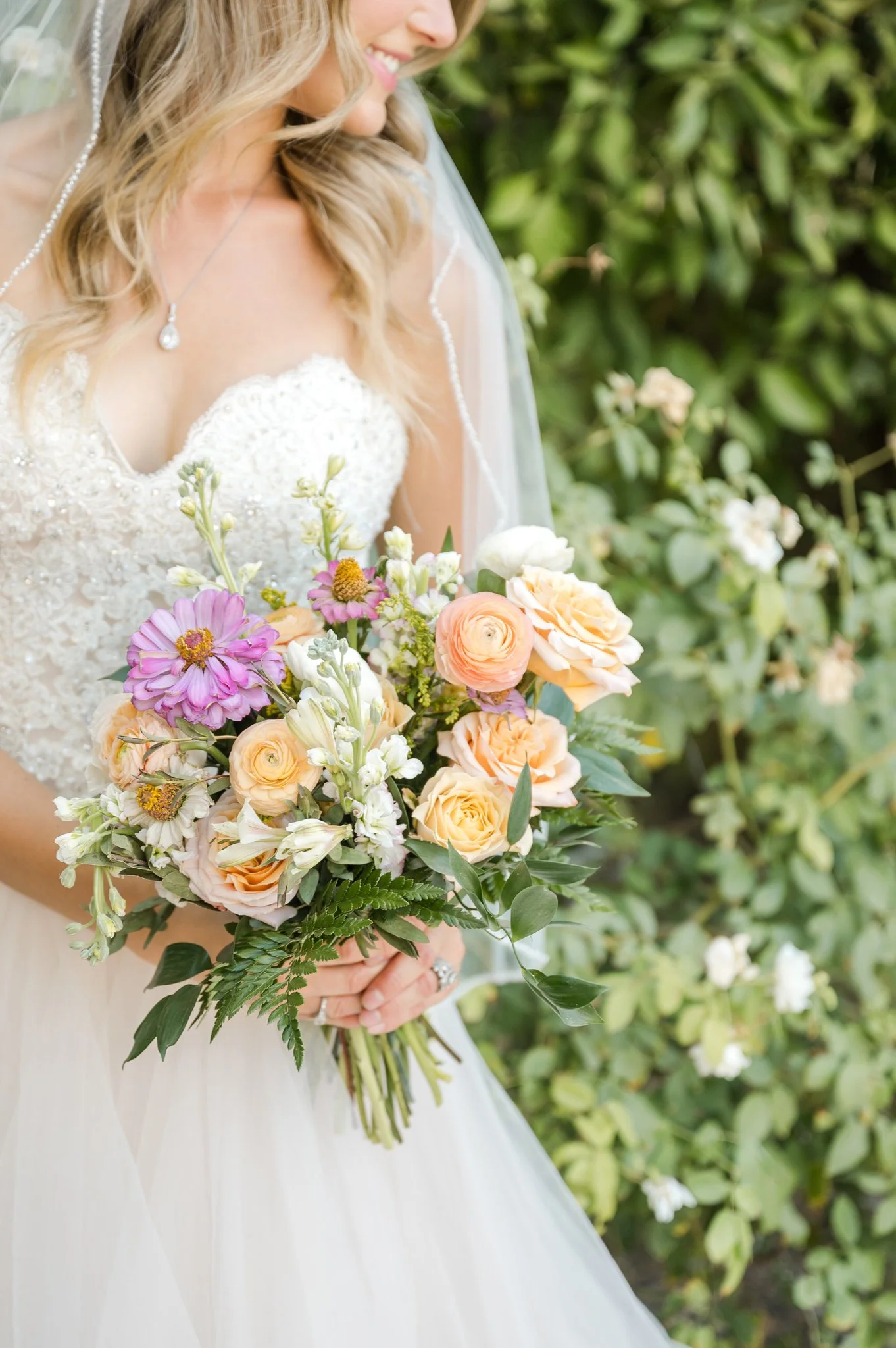 Colorful bridal bouquet featuring peach roses, pink and lavender flowers, yellow accents and organic greenery.