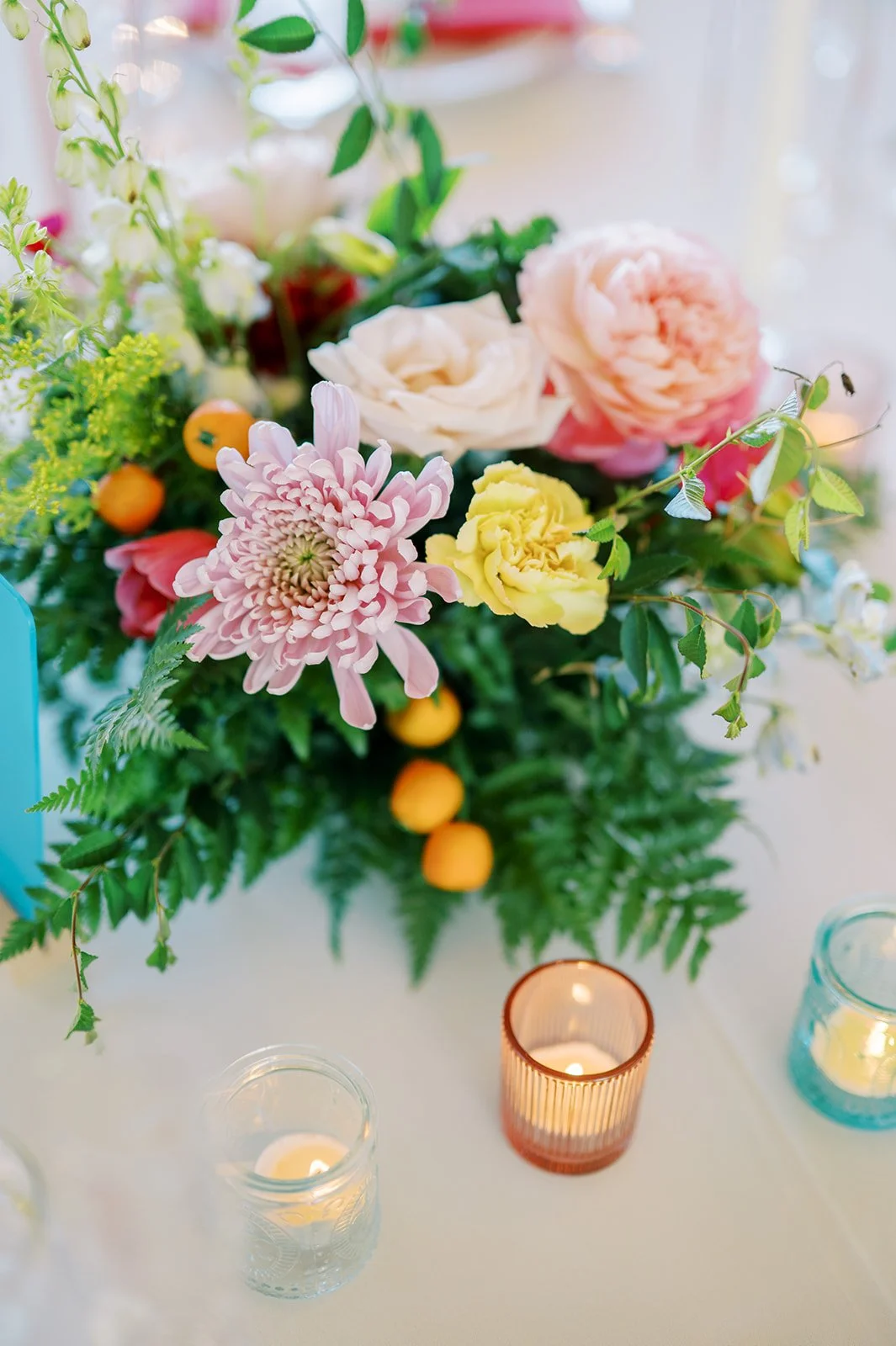 Close-up of a vibrant garden-style wedding bouquet with peach, pink, yellow and blue flowers and textured greenery.