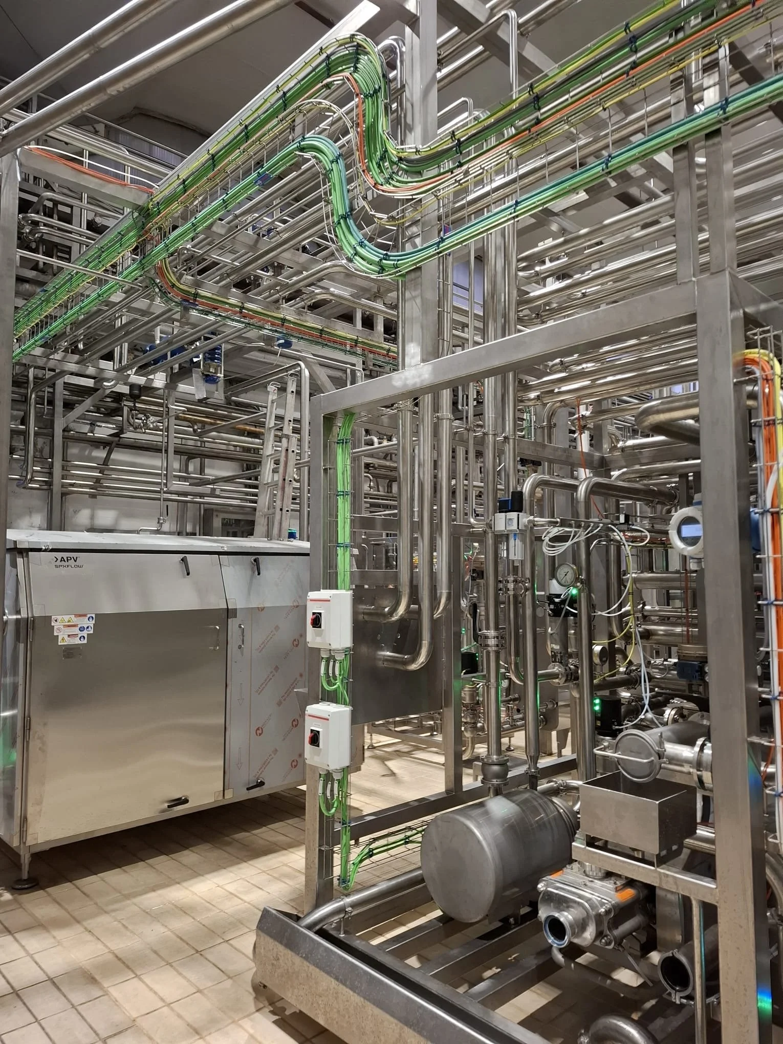 Industrial piping system with stainless steel pipes, valves, and equipment in a factory or processing plant.