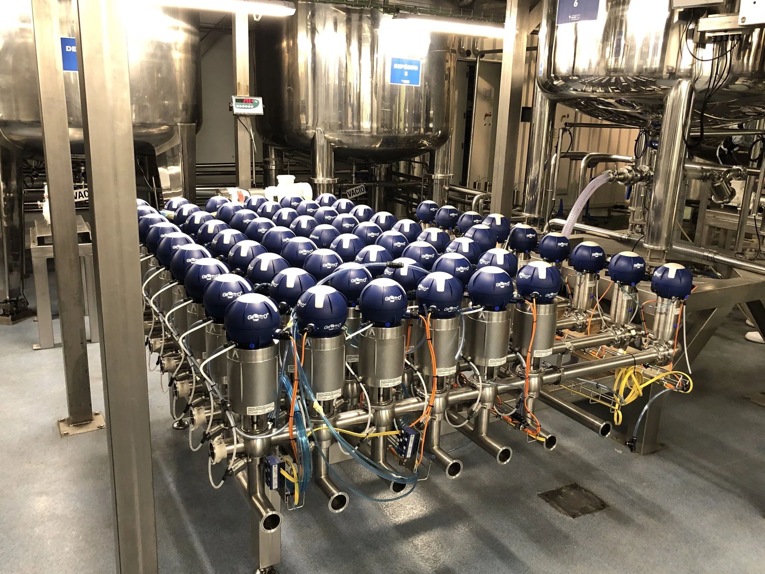 Industrial machinery with multiple blue components connected by stainless steel pipes and wires in a factory setting.