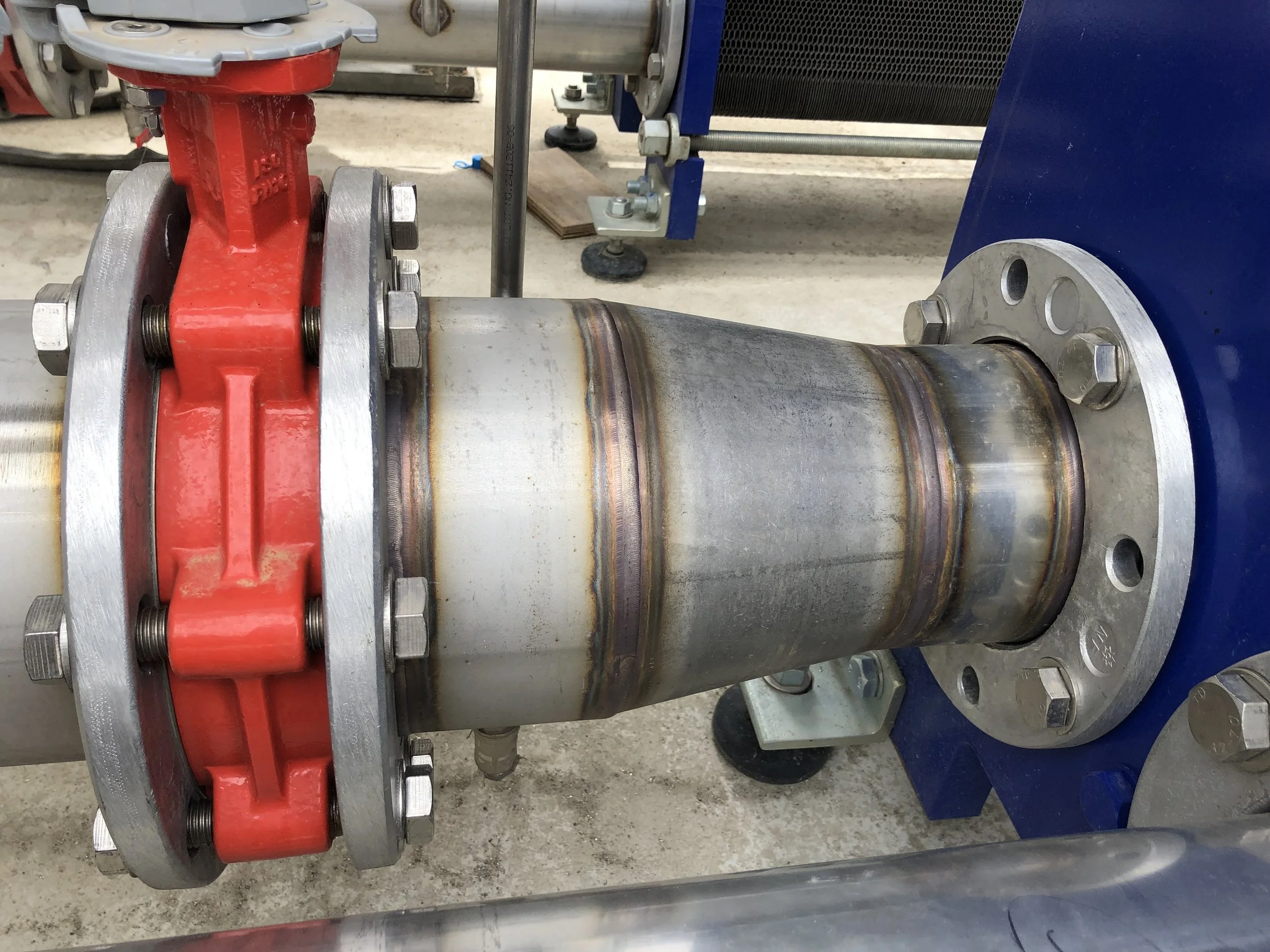 Industrial pipe with a red valve clamp and metal flange, installed on a concrete floor.