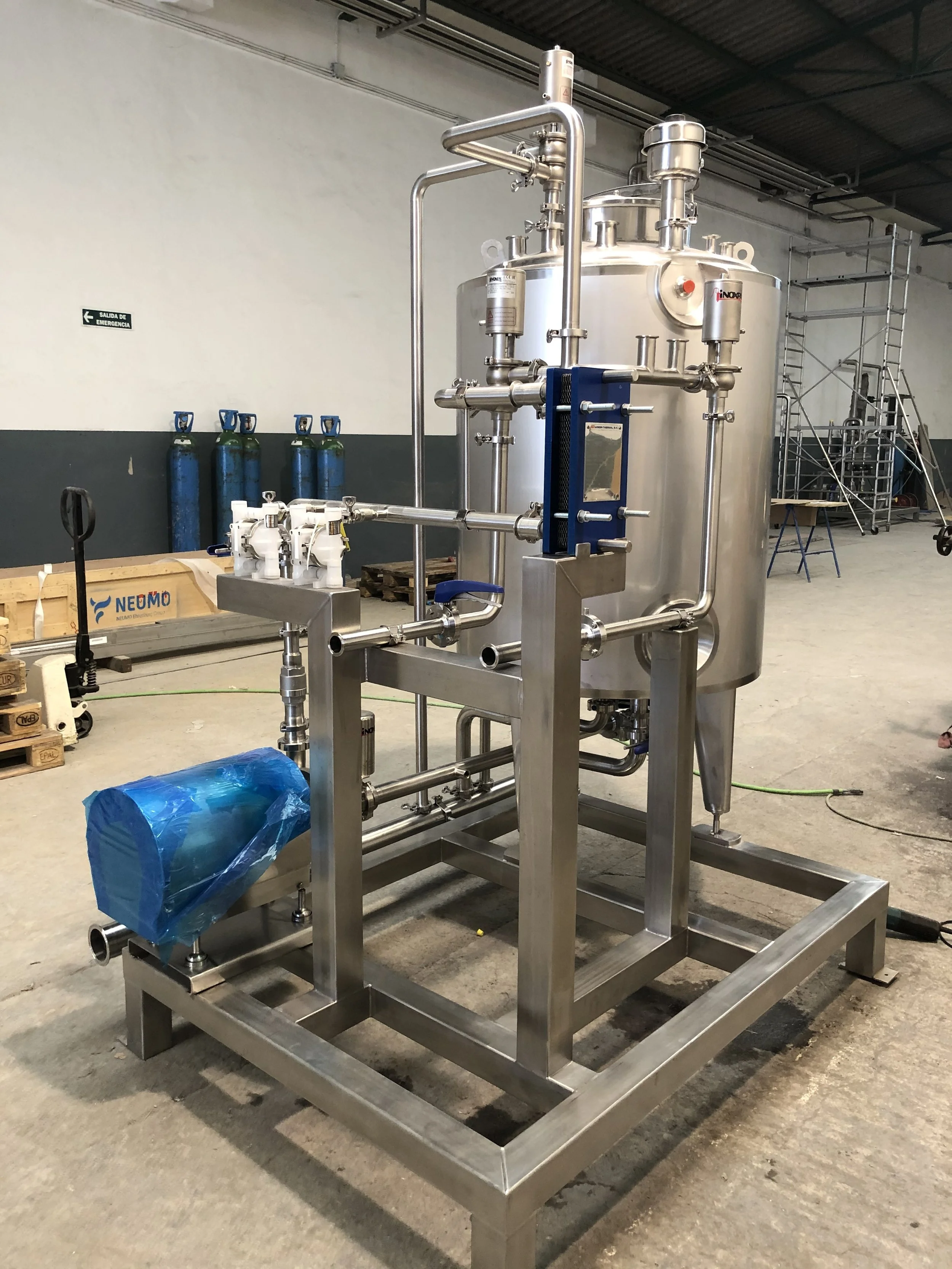 Stainless steel industrial process equipment with pipes, gauges, and valves, situated in a warehouse or industrial setting.