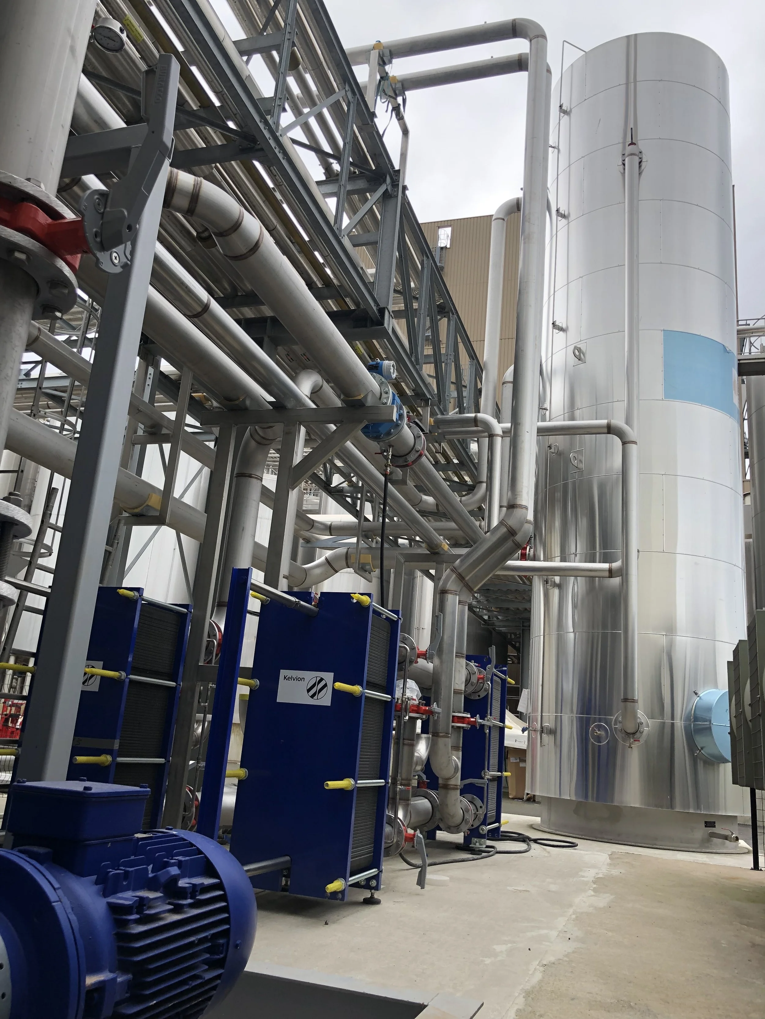 Industrial equipment with pipes, valves, and cooling units outside a factory or processing plant.