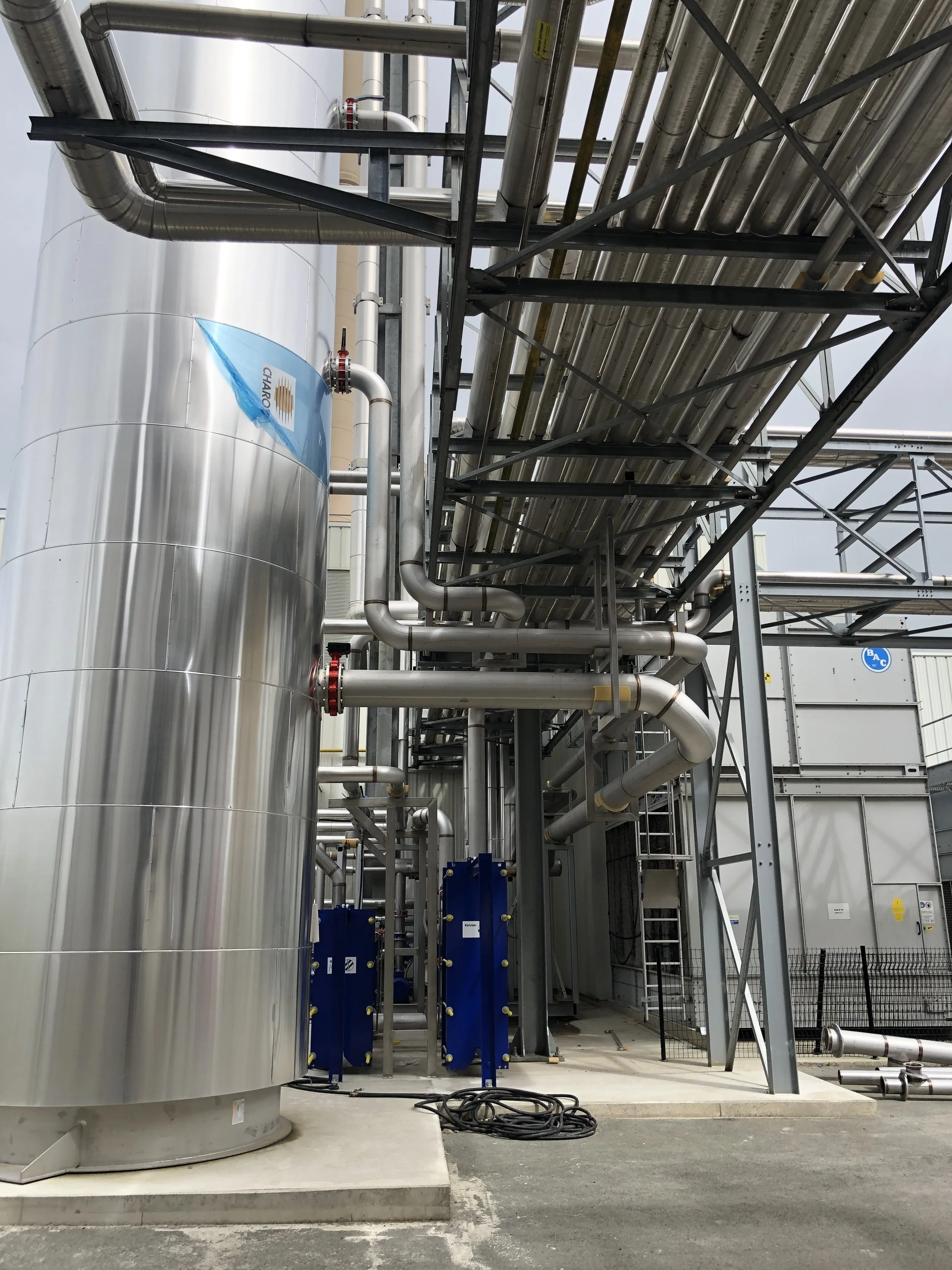 Industrial facility with large stainless steel tanks, pipes, and metal framework.