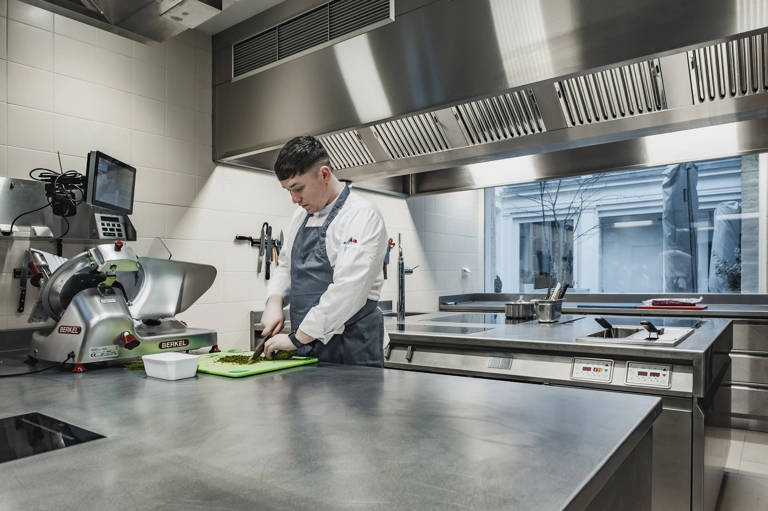 Kok in een moderne, professionele keuken snijdt groenten op een snijplank.