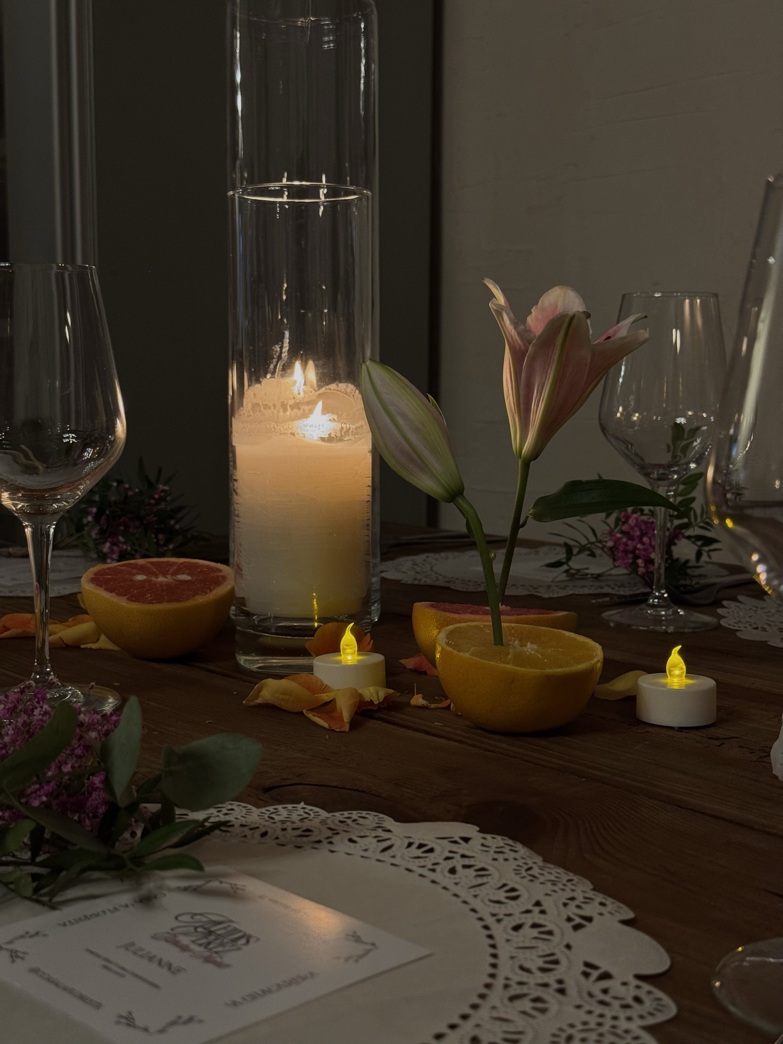 Mesa decorada con flores, velas y mitades de fruta, en un ambiente cálido y acogedor.