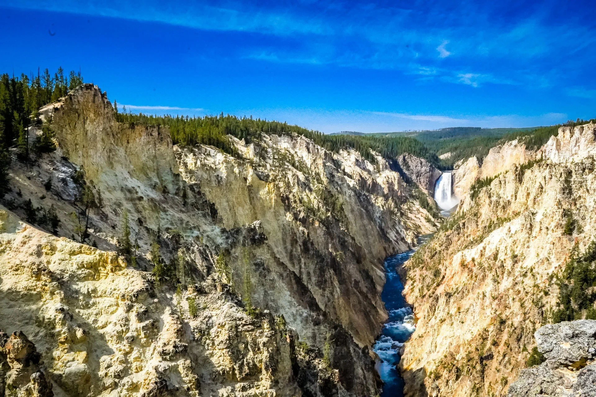 Scenic view of a deep canyon with rocky cliffs, a waterfall in the distance, and a river flowing through the bottom, with a clear blue sky overhead.