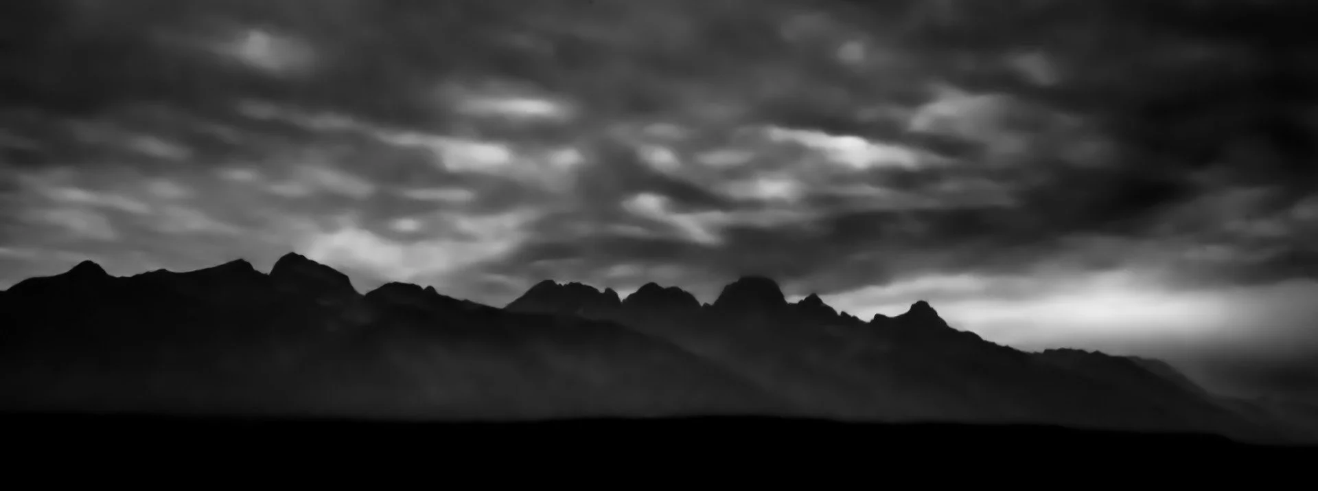 Black and white photograph of a mountain range under a cloudy sky.