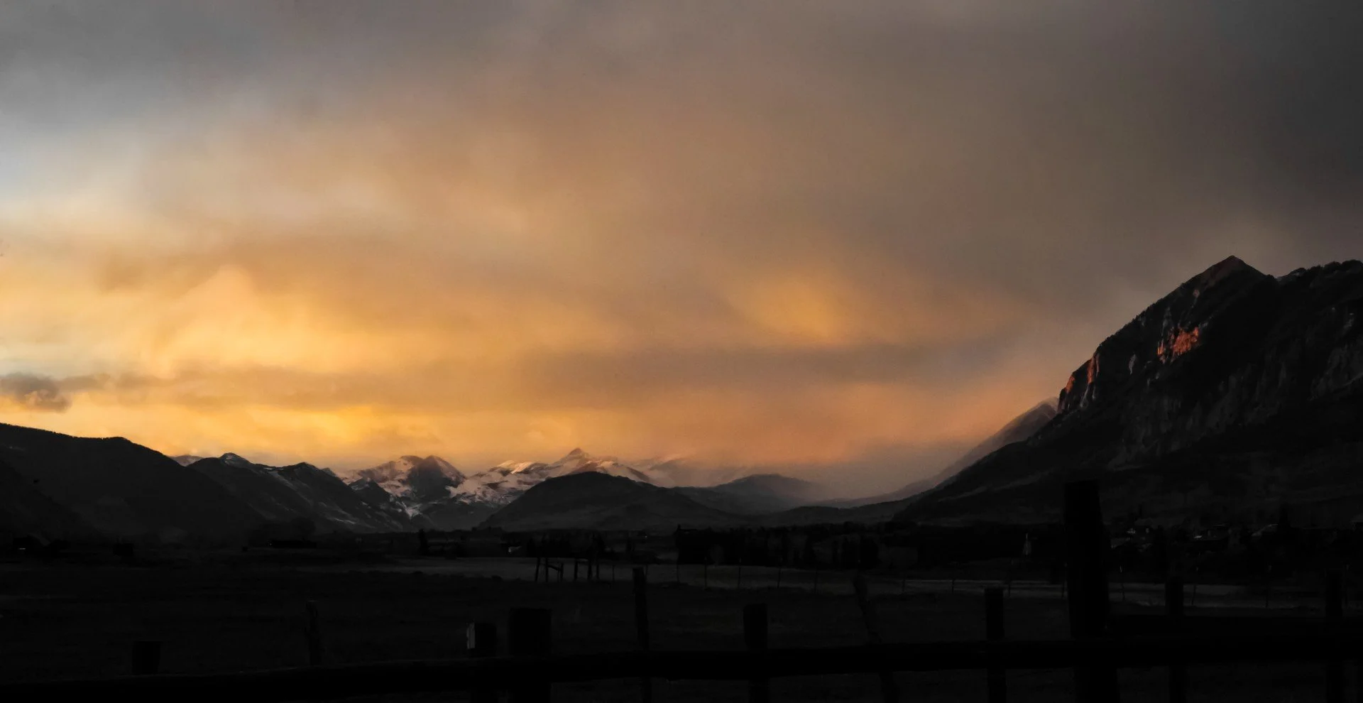 Sunset over a mountainous landscape with snow-capped peaks and a dark foreground.