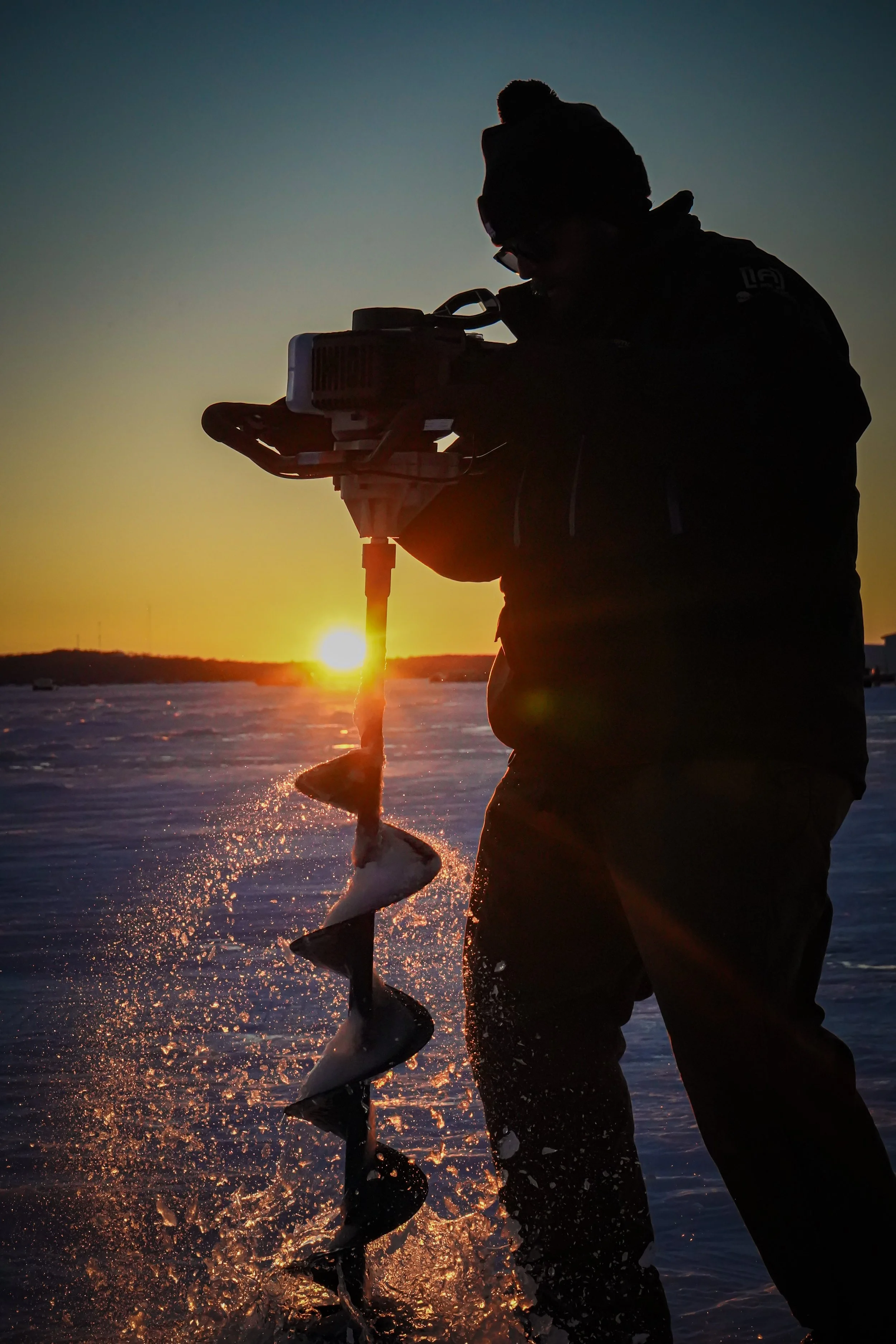Silhouette of a person operating a boat motor with a fish caught on the propeller, at sunset over a body of water.