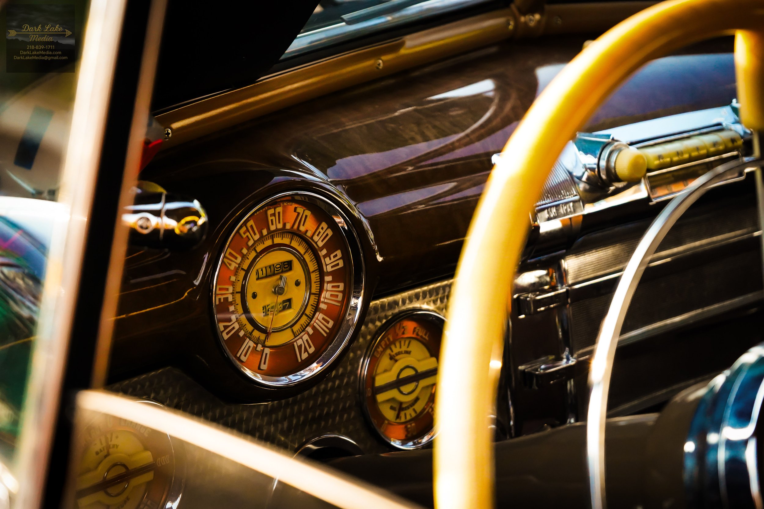 Close-up of vintage car dashboard showing speedometer and other gauges, with yellow steering wheel and metallic details.