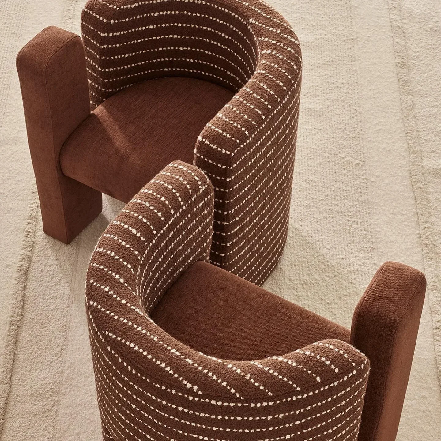 Two brown armchairs with patterned upholstery facing each other on a beige carpet.