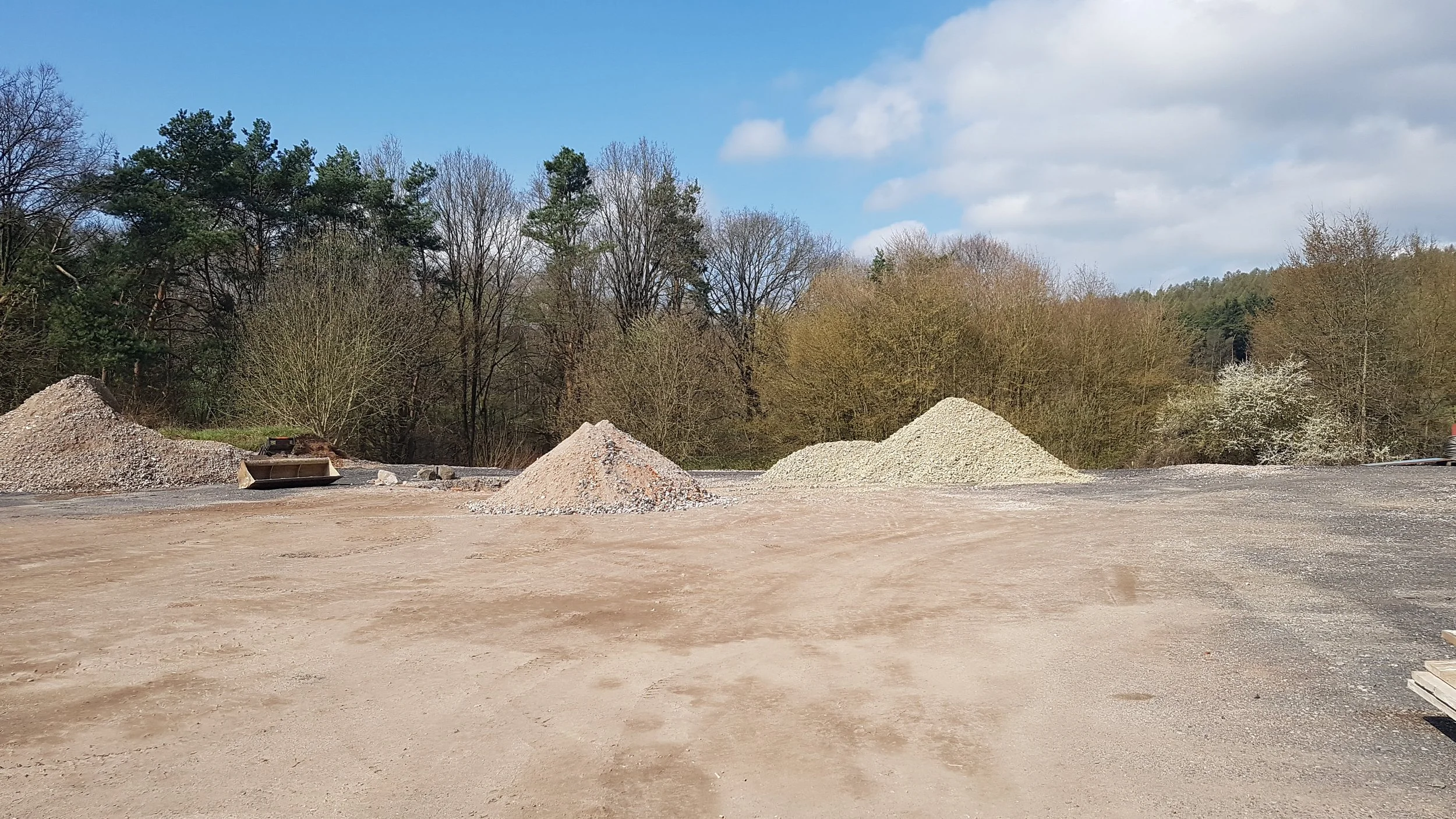 Baustelle mit mehreren Mülldecken und Kieshaufen, umgeben von Bäumen und Himmel.
