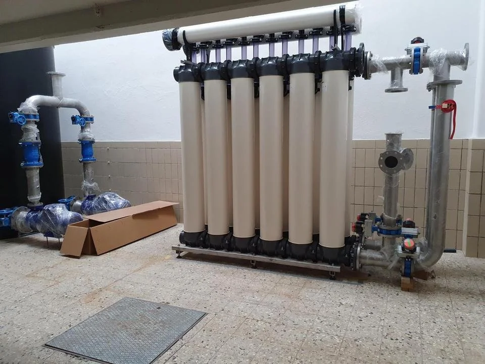 Industrieanlage mit vertikalen Rohrleitungen, Schläuchen und Ventilen in einem technischen Raum.