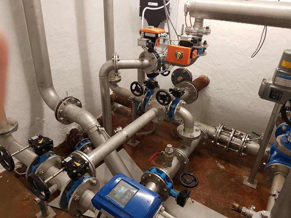 Ansicht von Rohrleitungen, Ventilen, Pumpen und Steuerelementen in einem technischen oder industriellen Gebäudeteil.