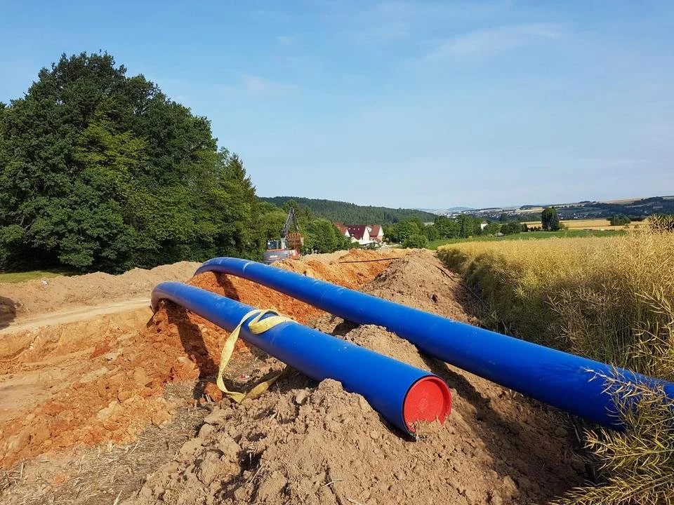 Bauarbeiten mit blauen Rohren in einer landwirtschaftlichen oder ländlichen Gegend, umgeben von Feldern und Bäumen.