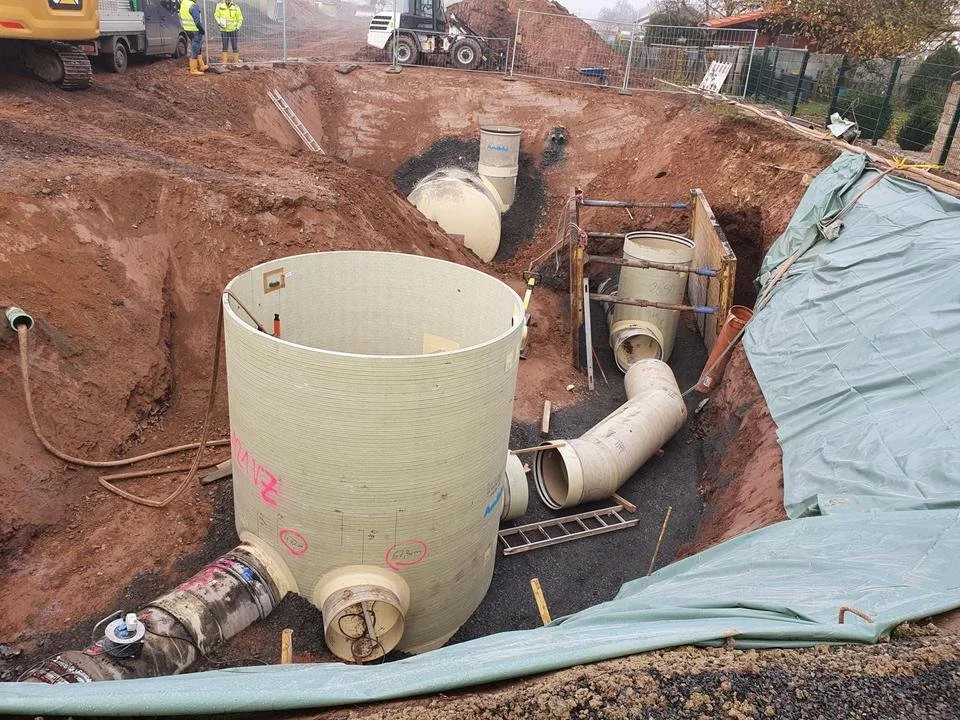 Bauarbeiten an einer unterirdischen Rohrleitung, mit großen Kunststoffrohren, die in einen tief ausgegrabenen Graben eingesetzt werden.