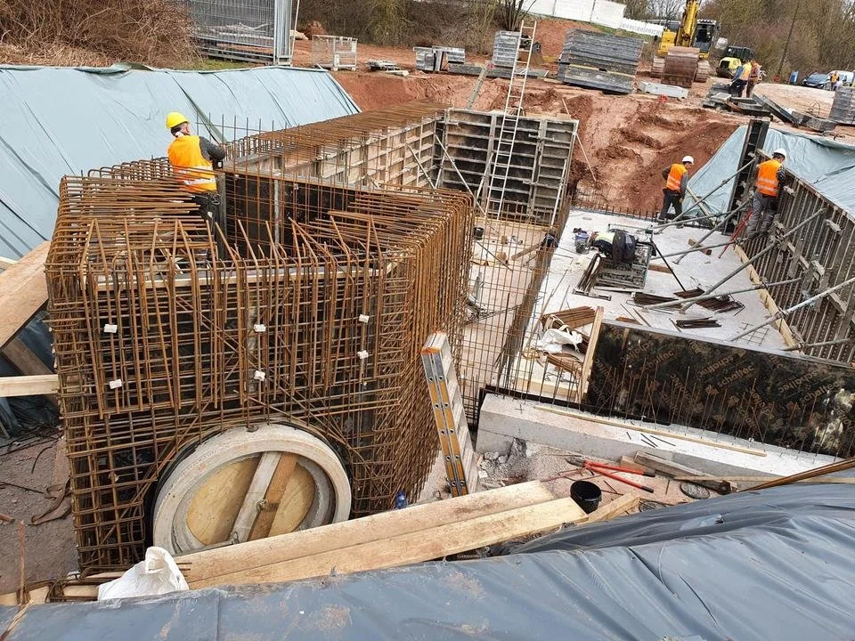 Bauarbeiter bei der Arbeit auf einer Baustelle, die mit Stahlbewehrungen und Schalungen für den Bau eines Fundaments oder einer Struktur ausgestattet ist.