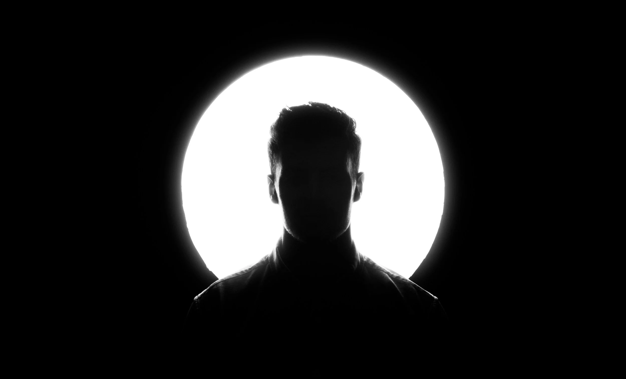 Silhouette of a person in front of a bright circular background, creating a high-contrast black-and-white image.