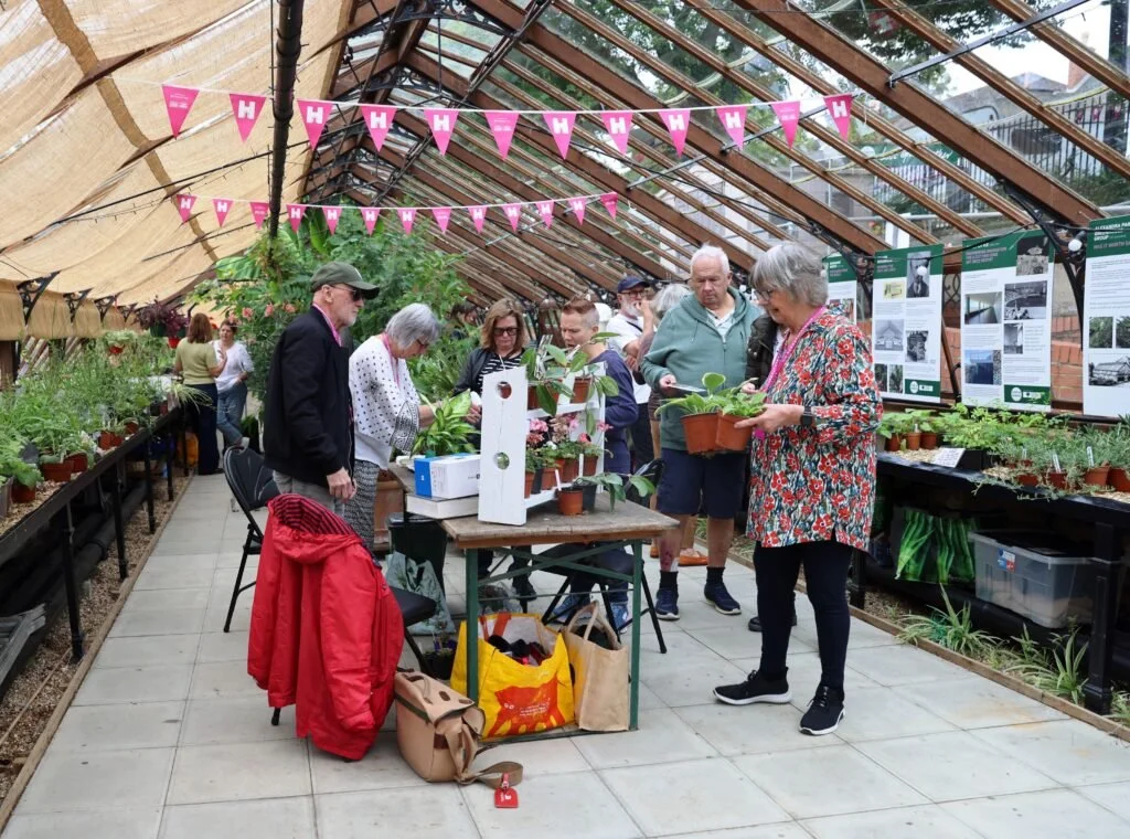 People browsing and purchasing plants inside a greenhouse decorated with pink banners.